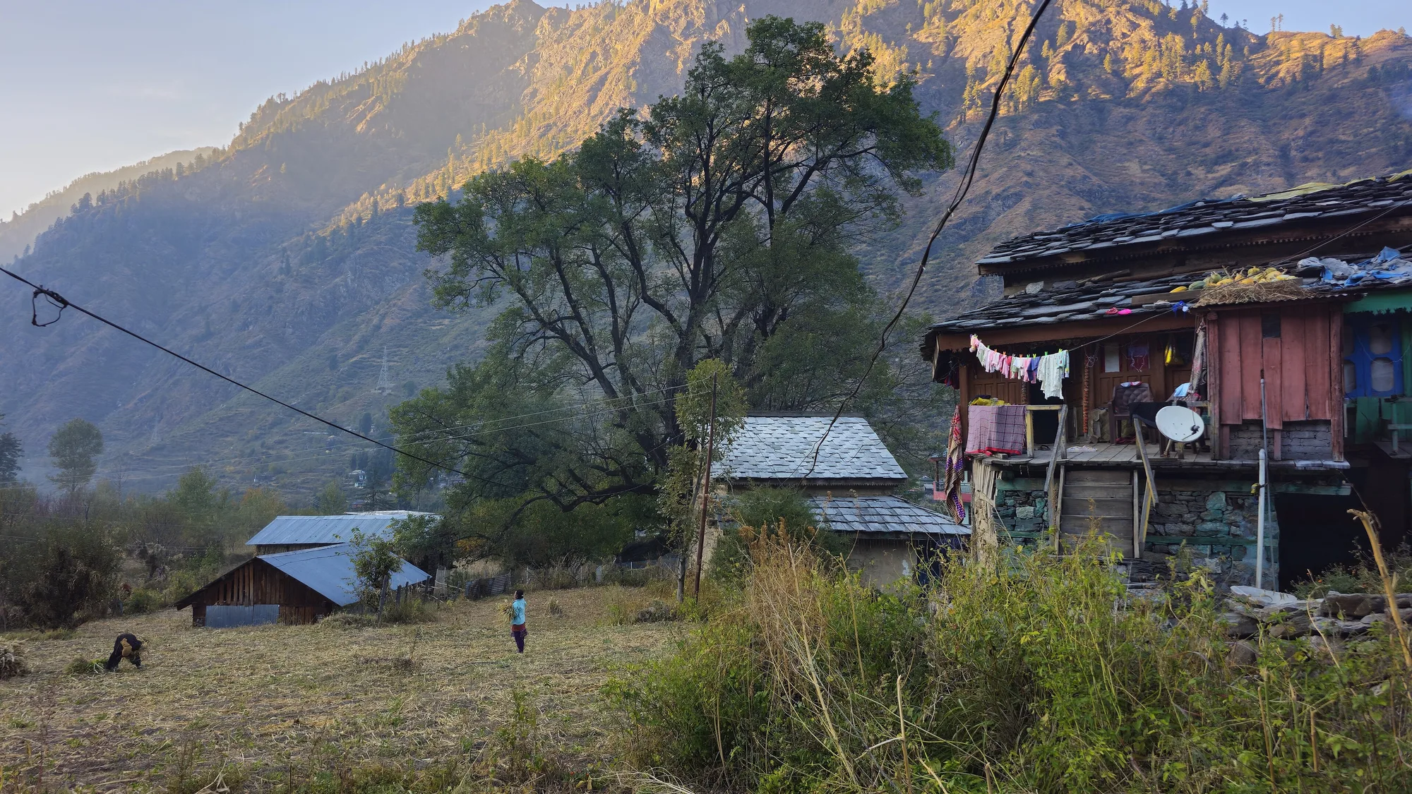 Wooden houses and an open field in Pulga village with autumn light on the mountains behind