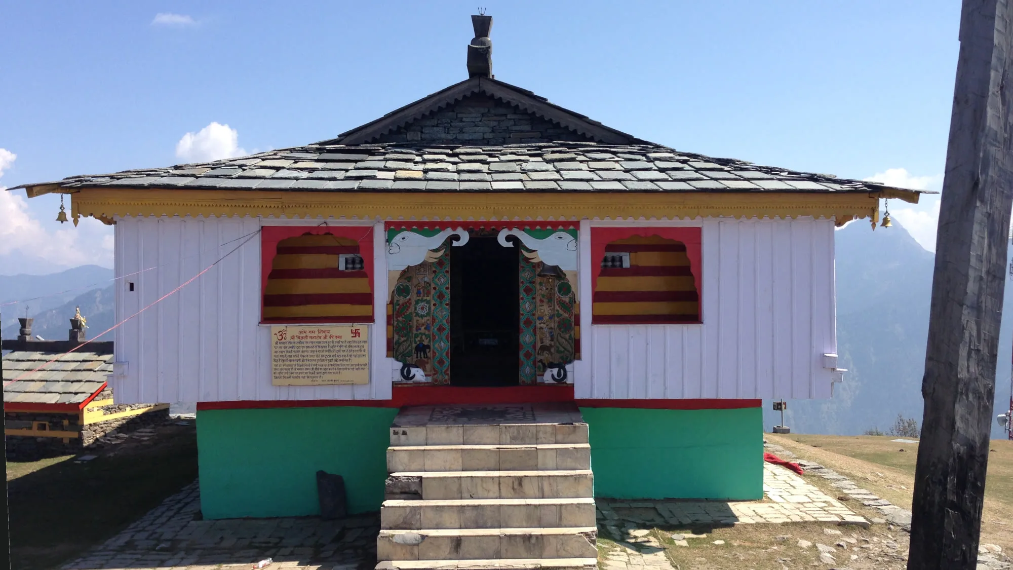 Bijli Mahadev temple in Kullu with a slate roof, white wooden walls and stone steps under a clear October sky