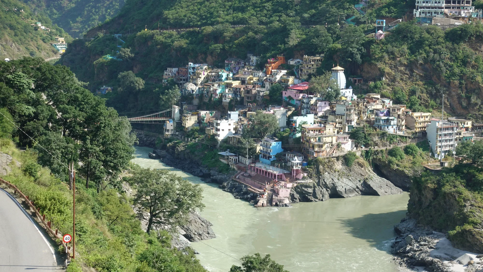 Devprayag town on a green hillside above the meeting of the Alaknanda and Bhagirathi rivers, with the highway curving past on the left