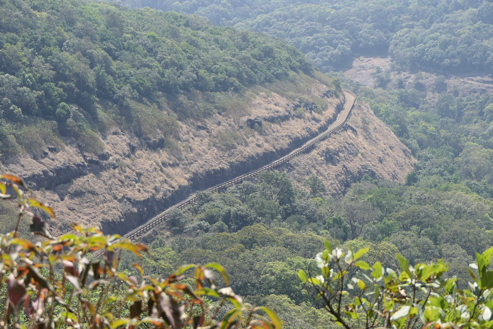 View from Panorama Point at Matheran over forested Western Ghats slopes, with the narrow-gauge toy train line curving along a bare hillside