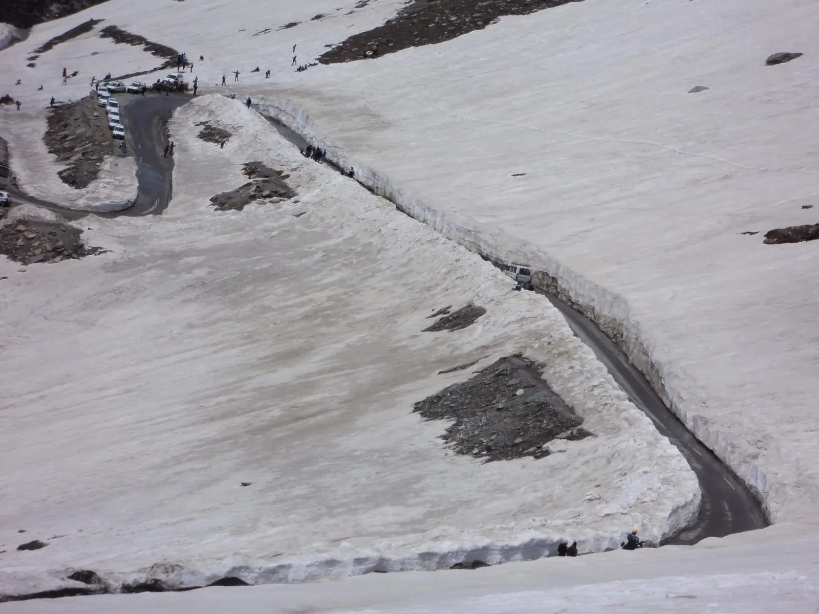 The road to Rohtang Pass from Manali winding across a snowfield, with patches of bare rock showing through the snow on a cloudy day
