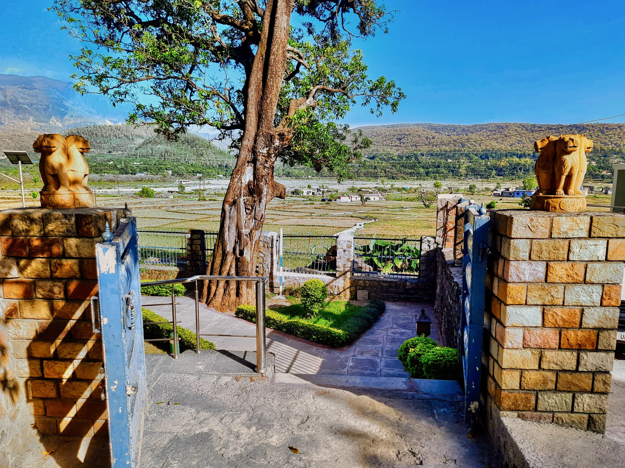 Gateway with stone lion pillars at the Ashoka rock edict site in Kalsi, with the Yamuna valley fields beyond, near Dehradun