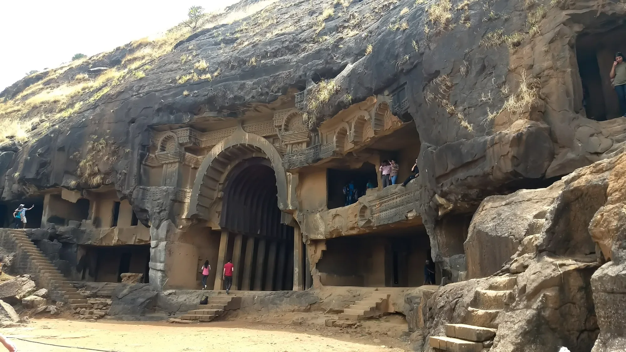 Side view of the Bhaja Caves cut into a basalt cliff, with the arched chaitya entrance and steps below