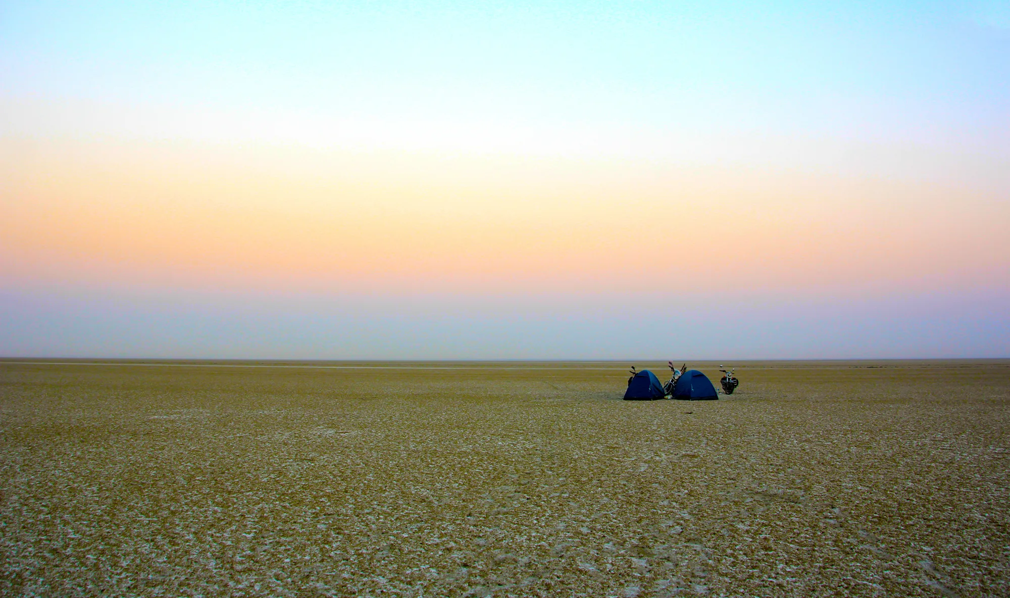Flat white salt bed of Sambhar Salt Lake stretching to the horizon under a pastel dawn sky, with two small tents in the distance