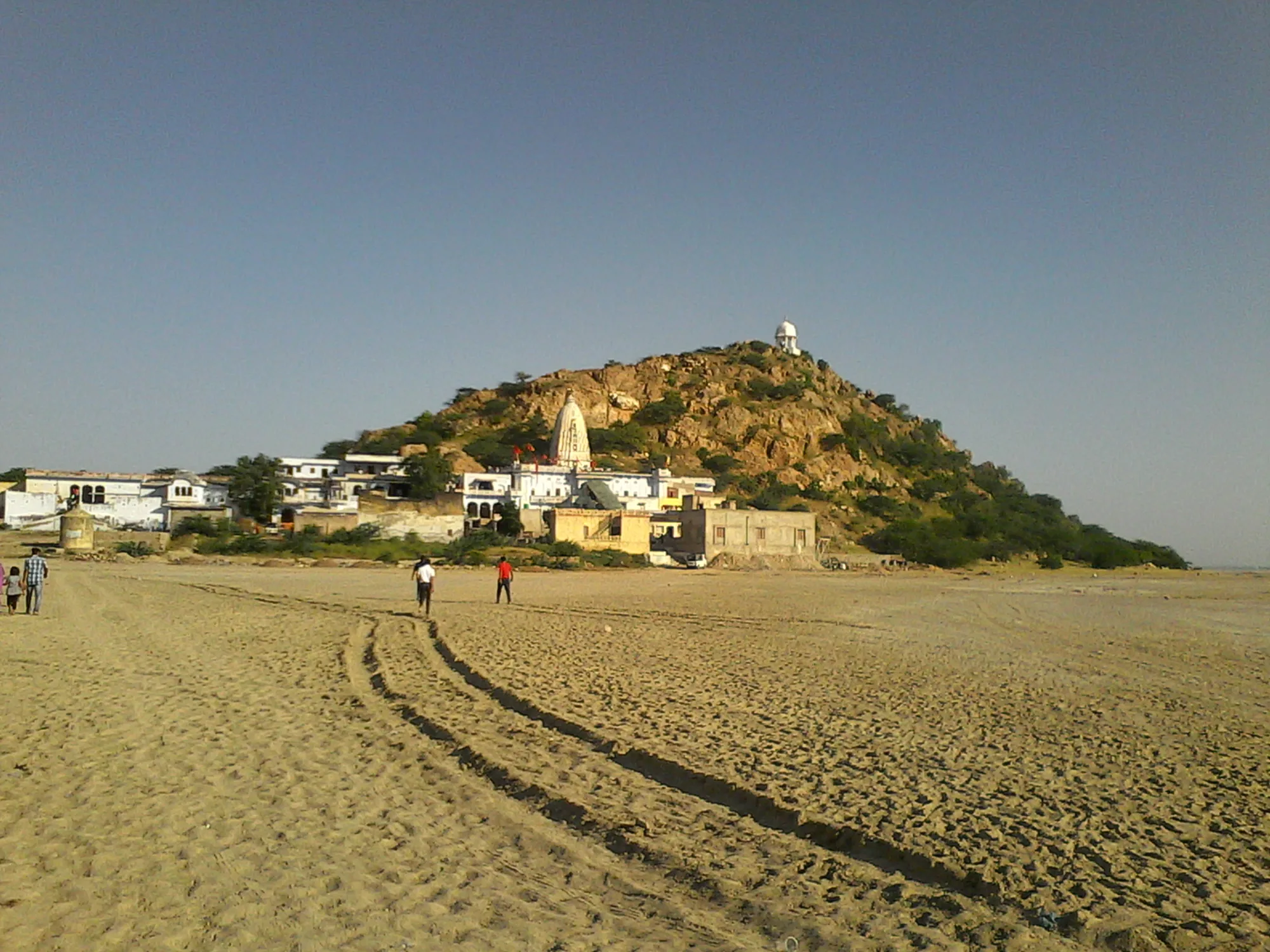 Shakambhari Mata temple on a rocky green hill at the edge of Sambhar Lake, with tyre tracks across the sandy lake bed in front