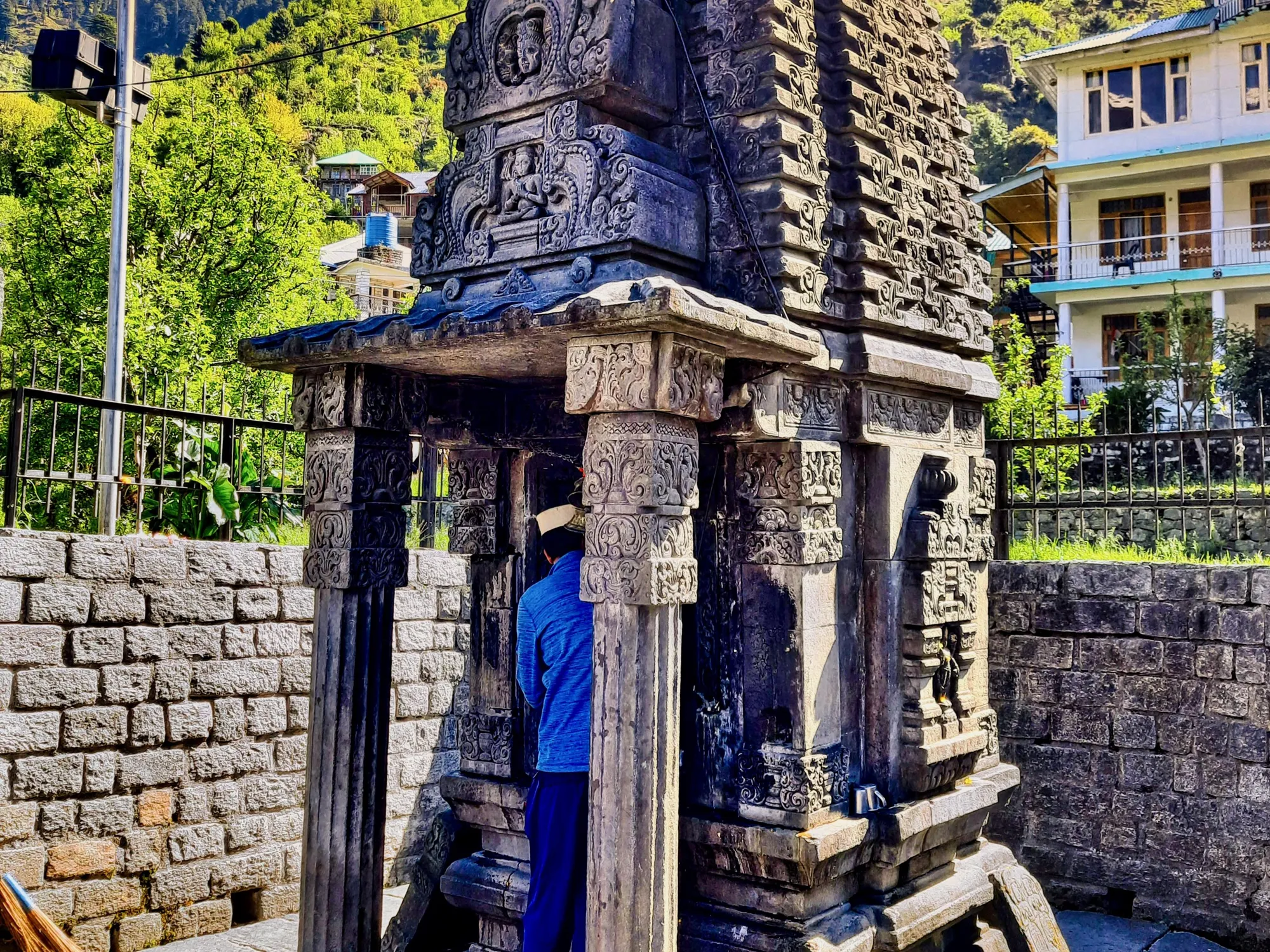 Carved grey stone Gauri Shankar Shiva temple in Jagatsukh village with green hills and houses behind