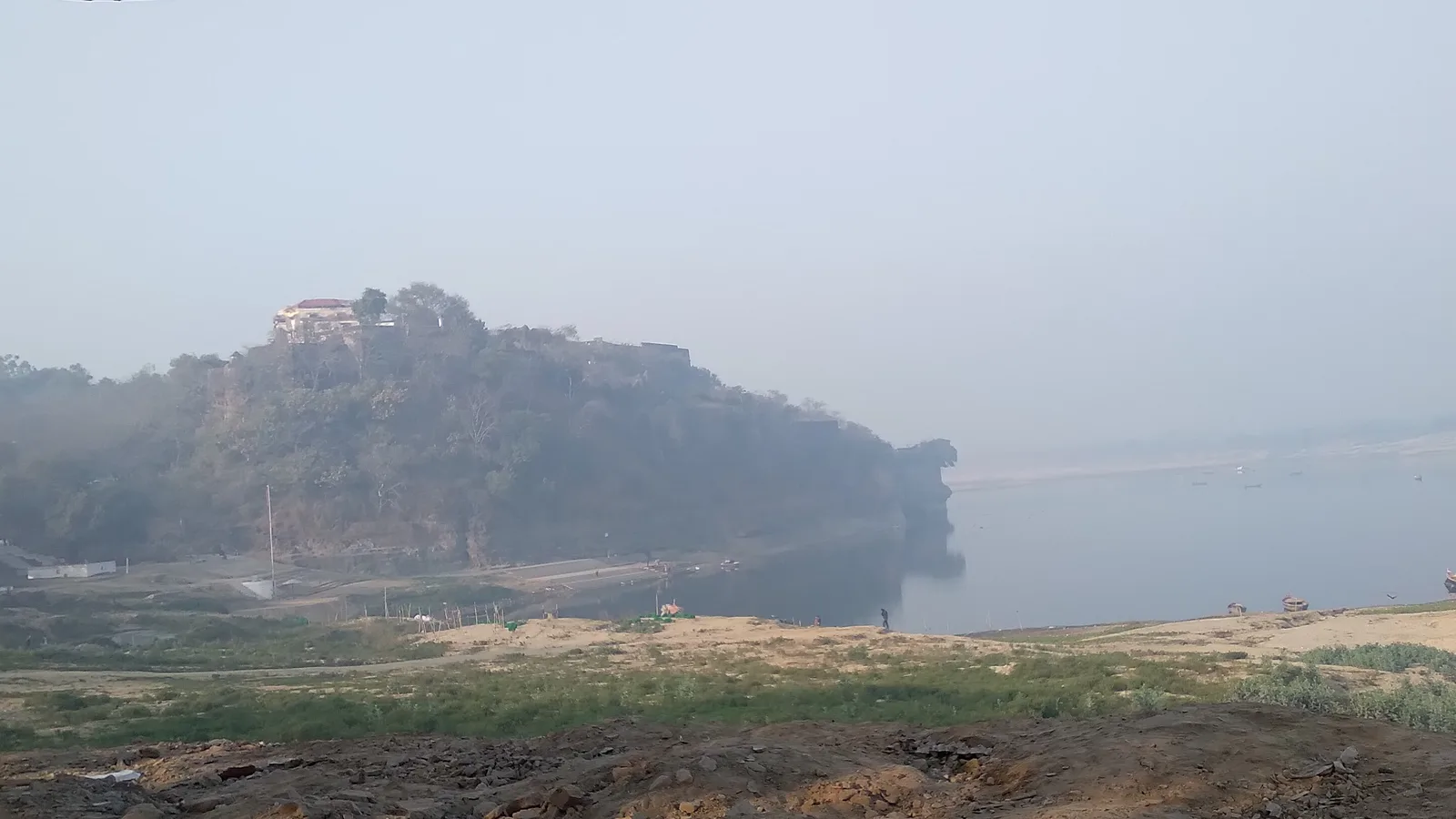 Distant view of Chunar Fort on a wooded hill rising above the misty Ganga and a sandy riverbank