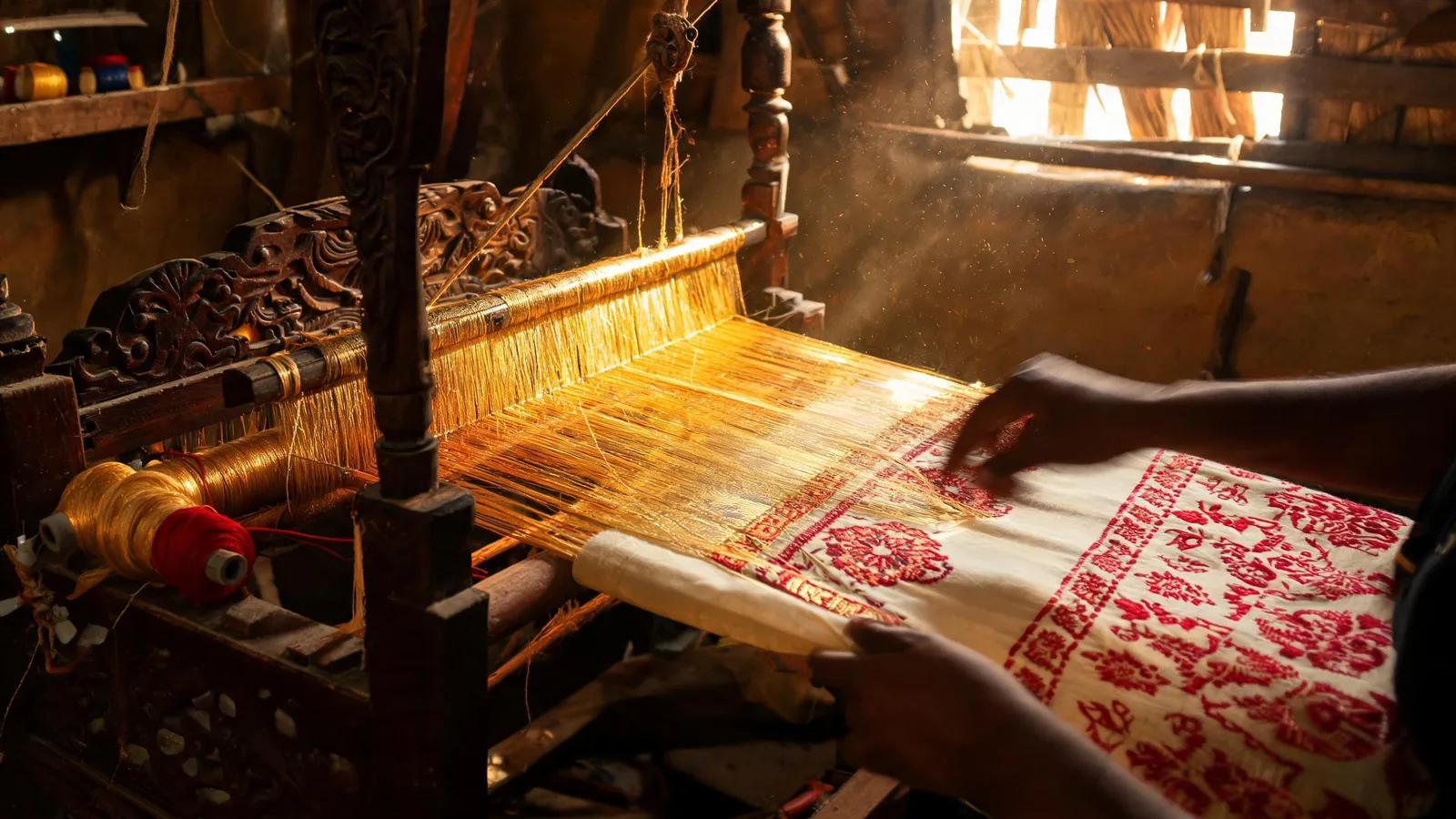 Traditional wooden handloom weaving cream silk with red motifs and golden threads in an Assamese workshop