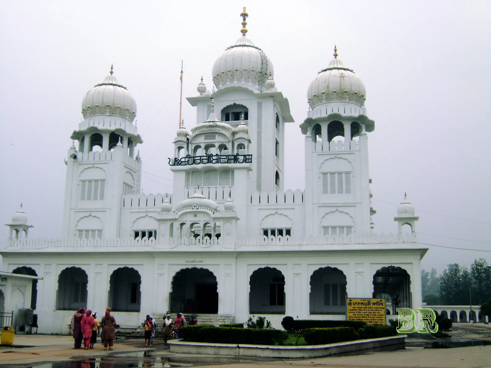 White Gurdwara Patalpuri Sahib with several domes on a hazy day at Kiratpur Sahib, Punjab, with visitors in front