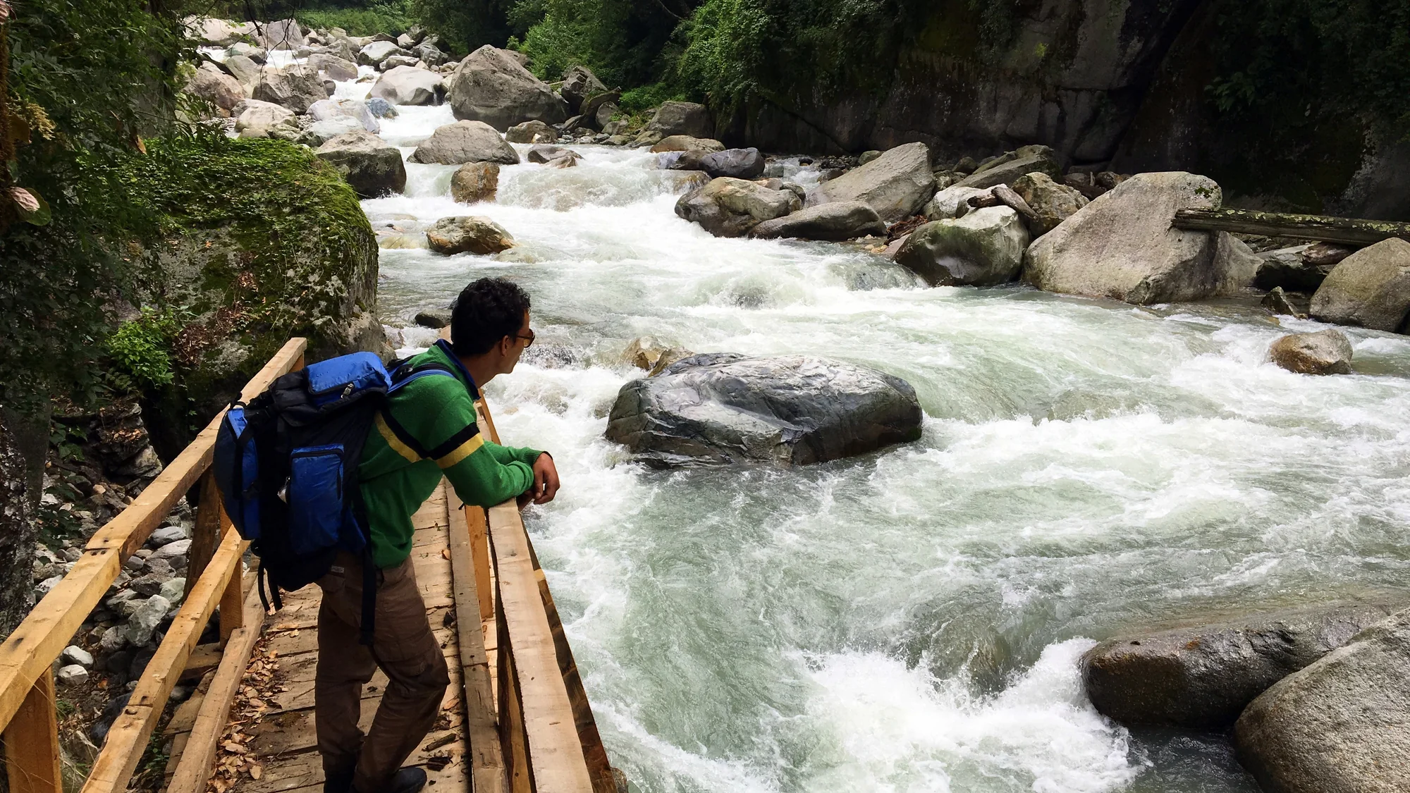 A rushing Tirthan River with pale glacial water and boulders in a green Himachal valley, the kind of stop a bike rental in Bhuntar puts within a day's ride