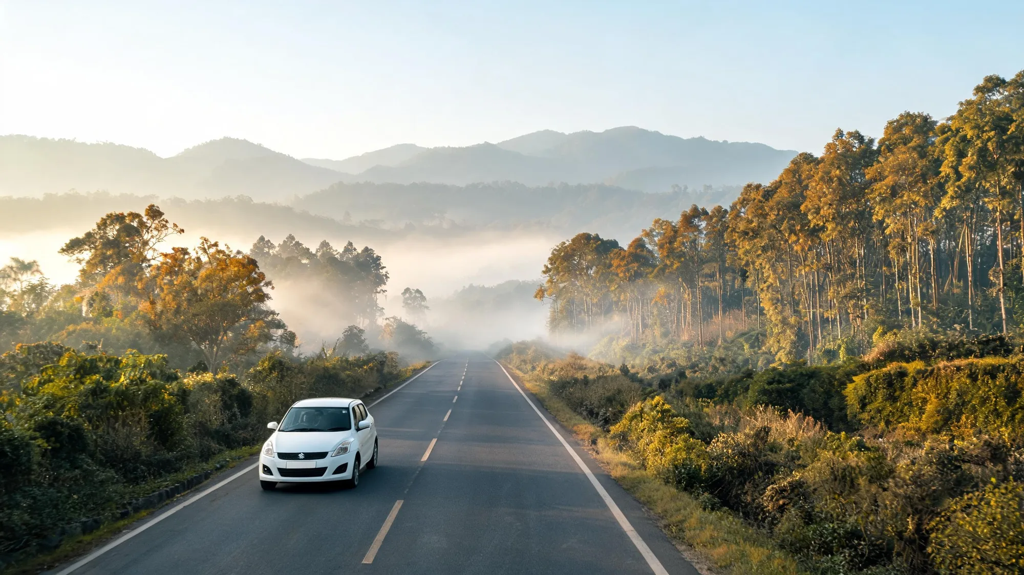 Self-drive car rental in Dehradun: white hatchback on a misty autumn foothill highway toward Ramnagar and Corbett