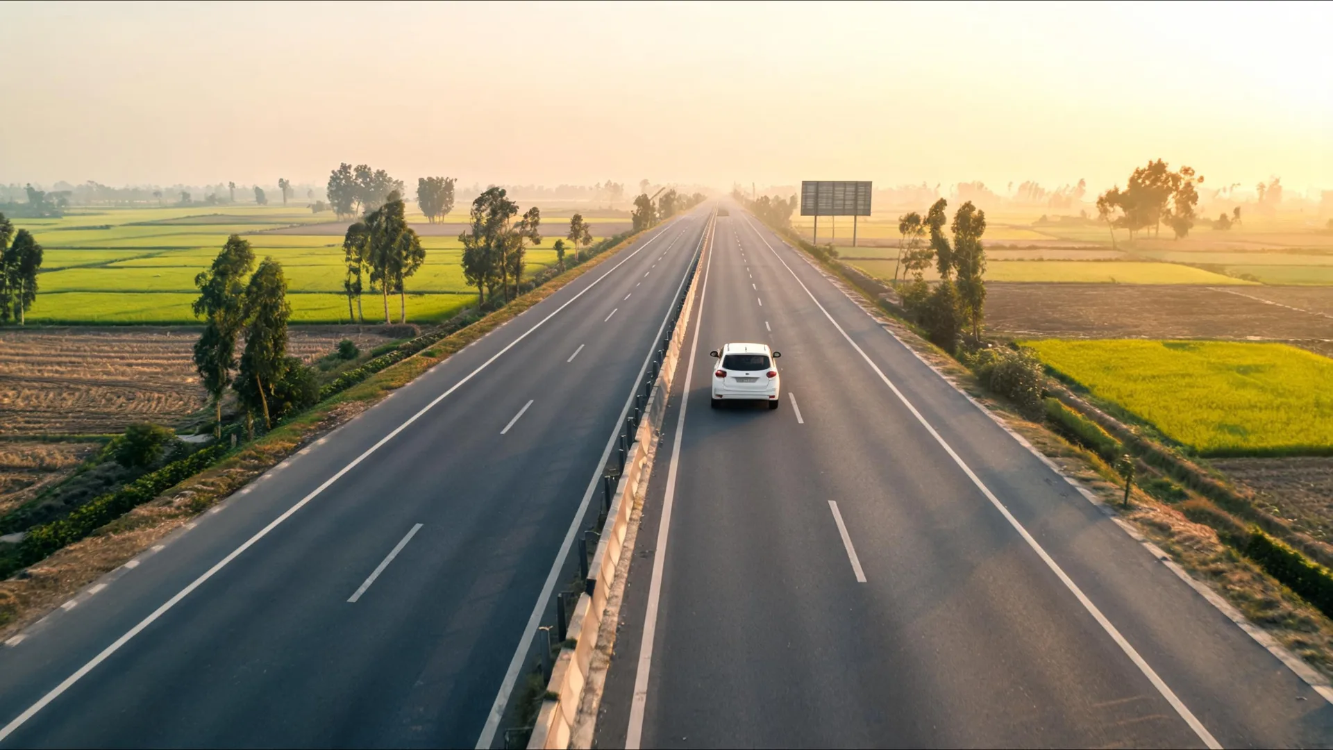 White self-drive rental car on an empty NH44 Grand Trunk Road through Haryana farmland at sunrise, on a self-drive car rental in Delhi day trip to Kurukshetra