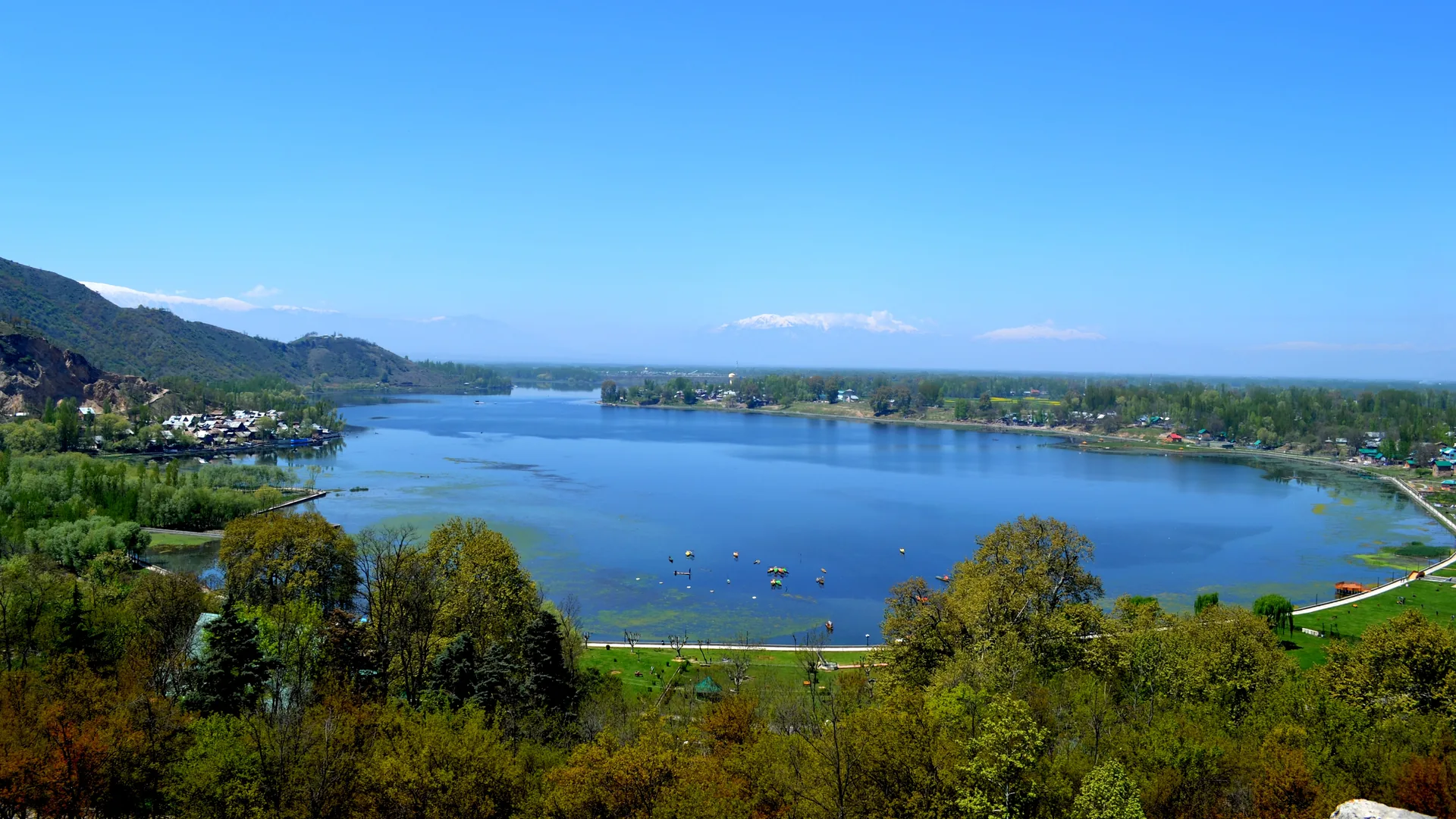 Manasbal Lake seen from a hillside, with wooded hills on the left and villages along the shore, a short drive on a car rental in Srinagar