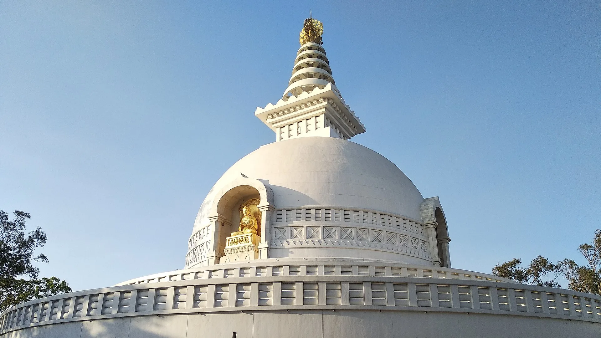 White Vishwa Shanti Stupa with a golden Buddha statue on Ratnagiri hill in Rajgir under a clear blue sky