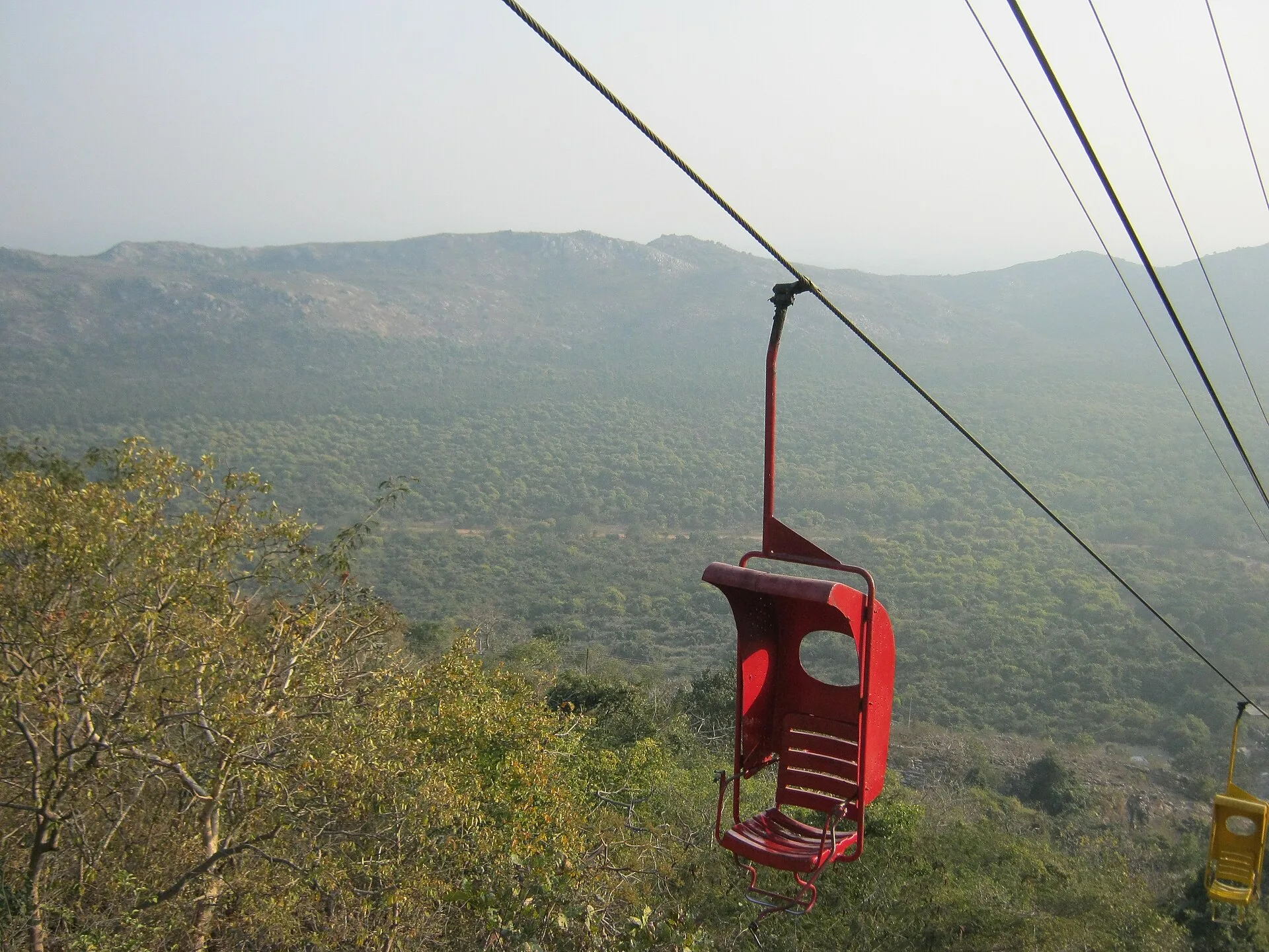 Empty red single-seat chair of the Rajgir ropeway above forested hills on the way to the Vishwa Shanti Stupa