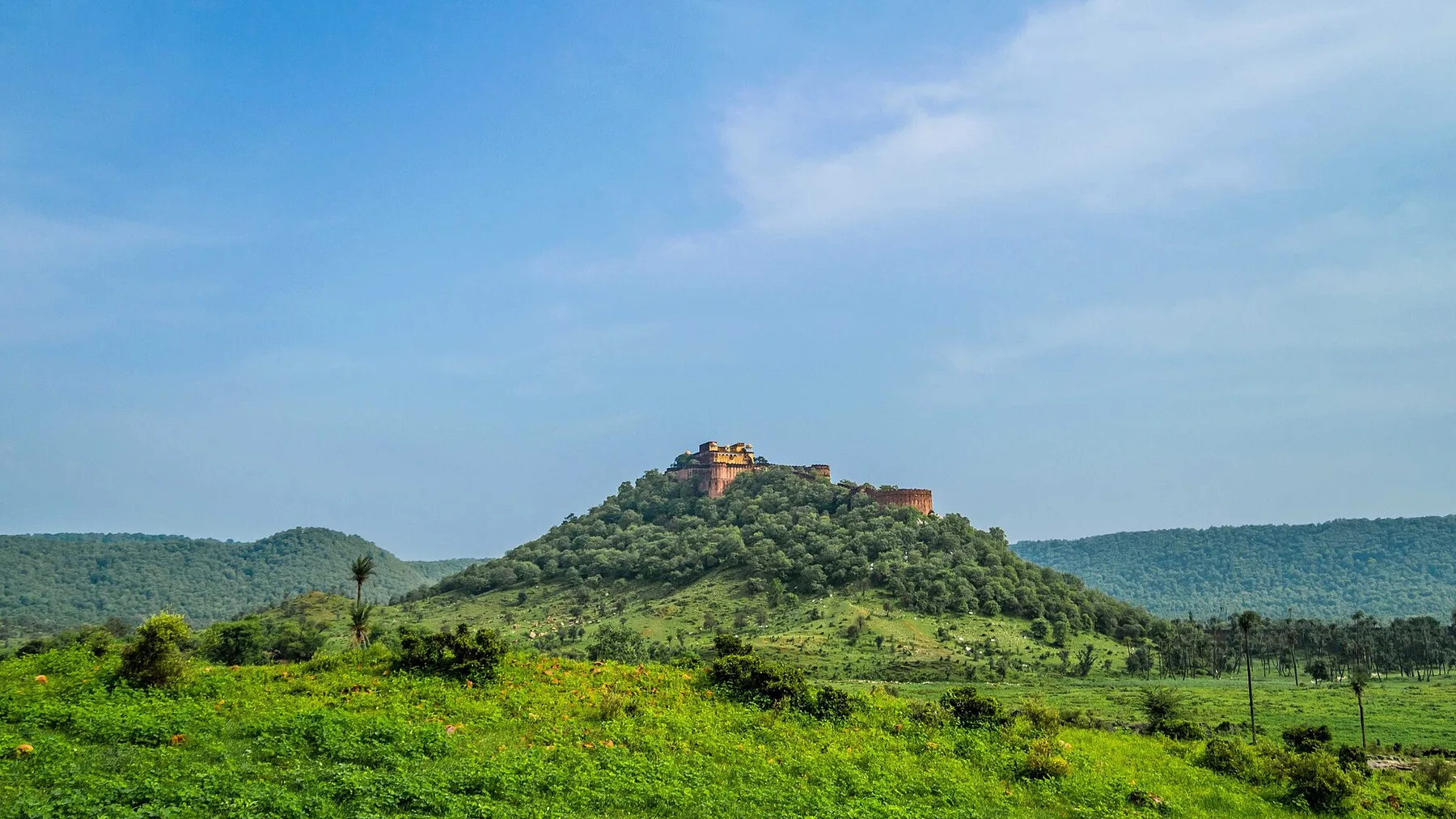 Kankwari Fort on a green hill inside Sariska Tiger Reserve under a blue sky, a trip by self-drive car rental in Gurugram
