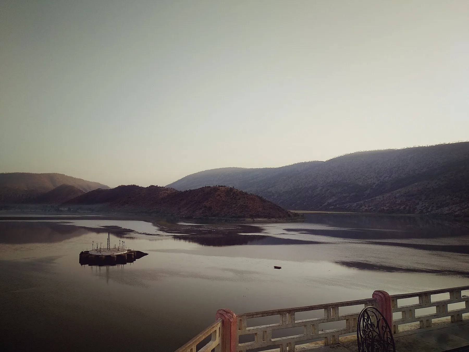 Siliserh Lake near Alwar at dusk, with the Aravalli hills reflected in still water beyond the palace terrace railing