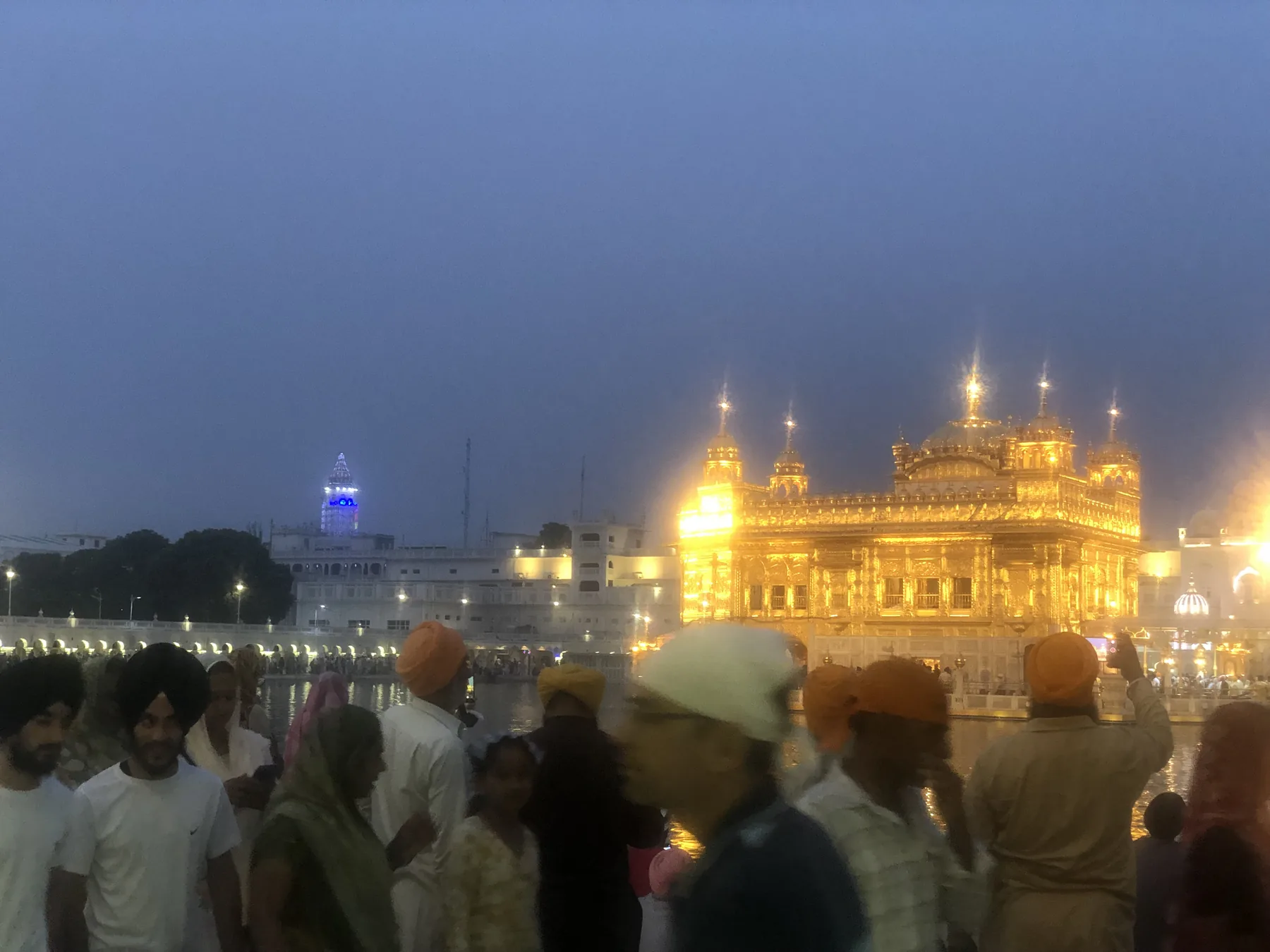 Harmandir Sahib illuminated at night with pilgrims in the foreground beside the sarovar in Amritsar