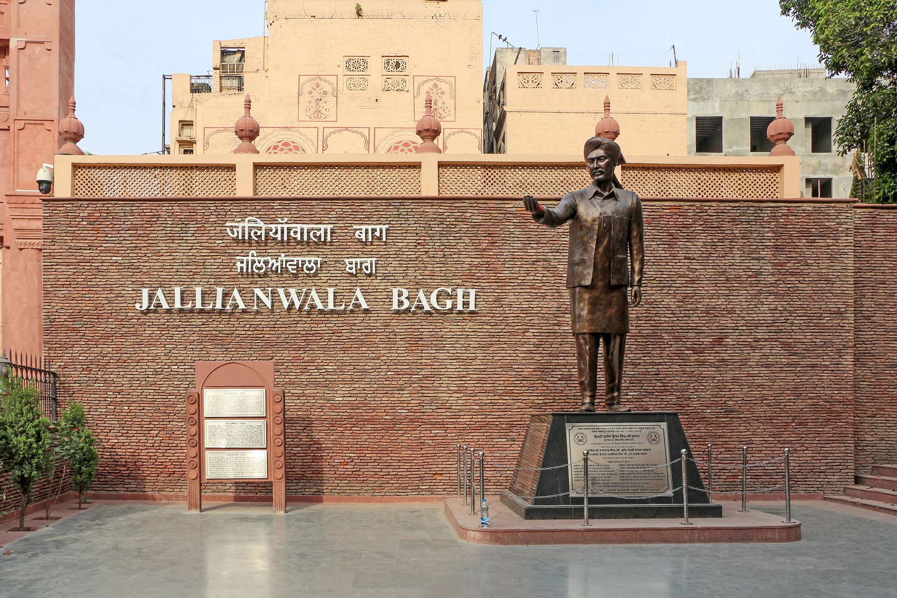 Bronze statue and brick wall reading Jallianwala Bagh at the memorial entrance in Amritsar