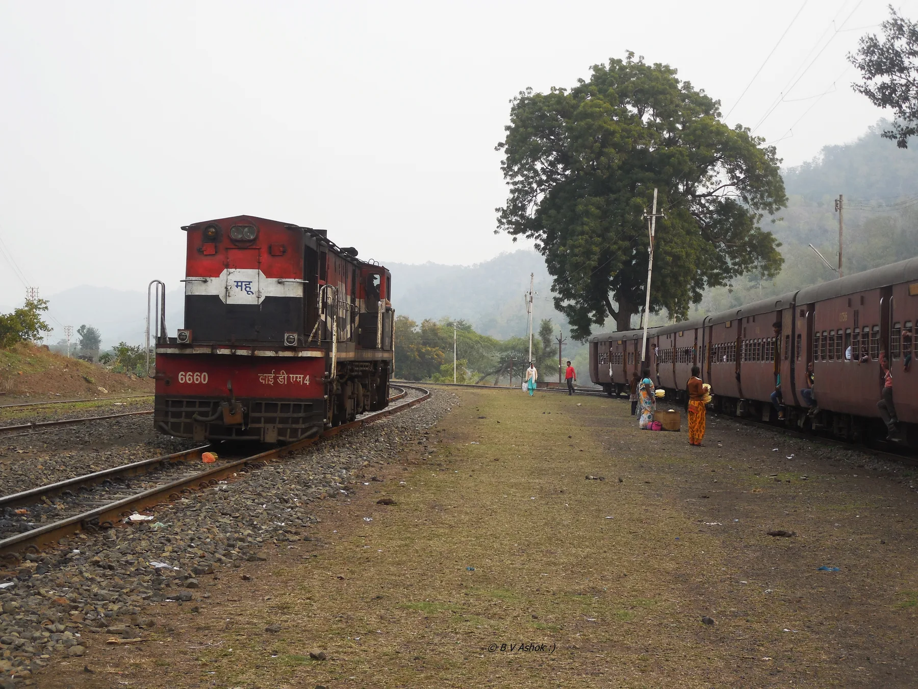 A red metre-gauge diesel locomotive beside a passenger train at Kalakund station in the forested hills south of Mhow