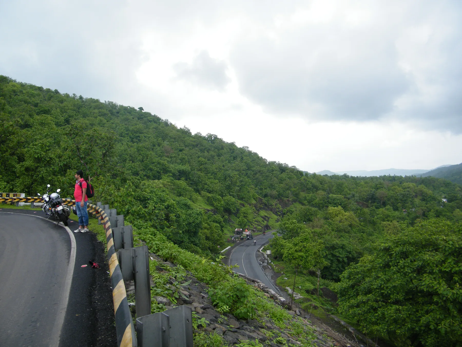 A ghat road looping down a forested hillside near Mhow towards Choral, with a rider parked at a bend