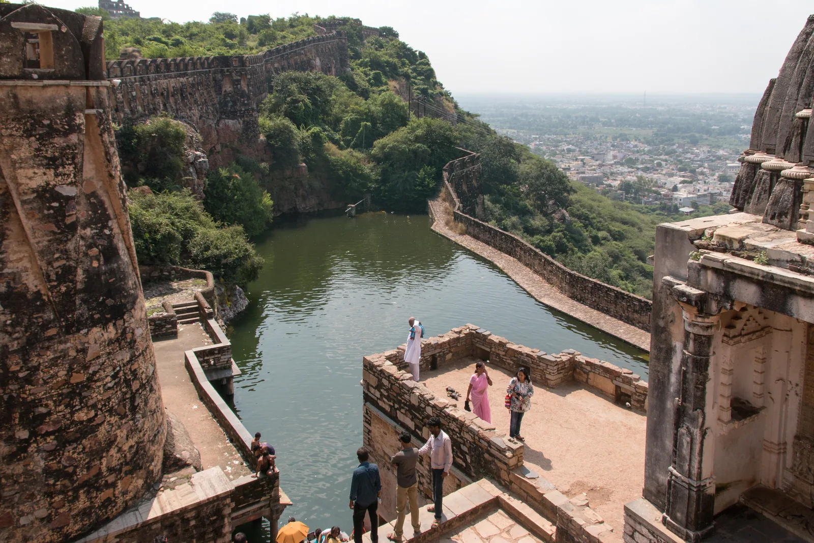 Gaumukh reservoir at Chittorgarh Fort, a green spring-fed tank below the fort walls with the town spread out on the plain beyond
