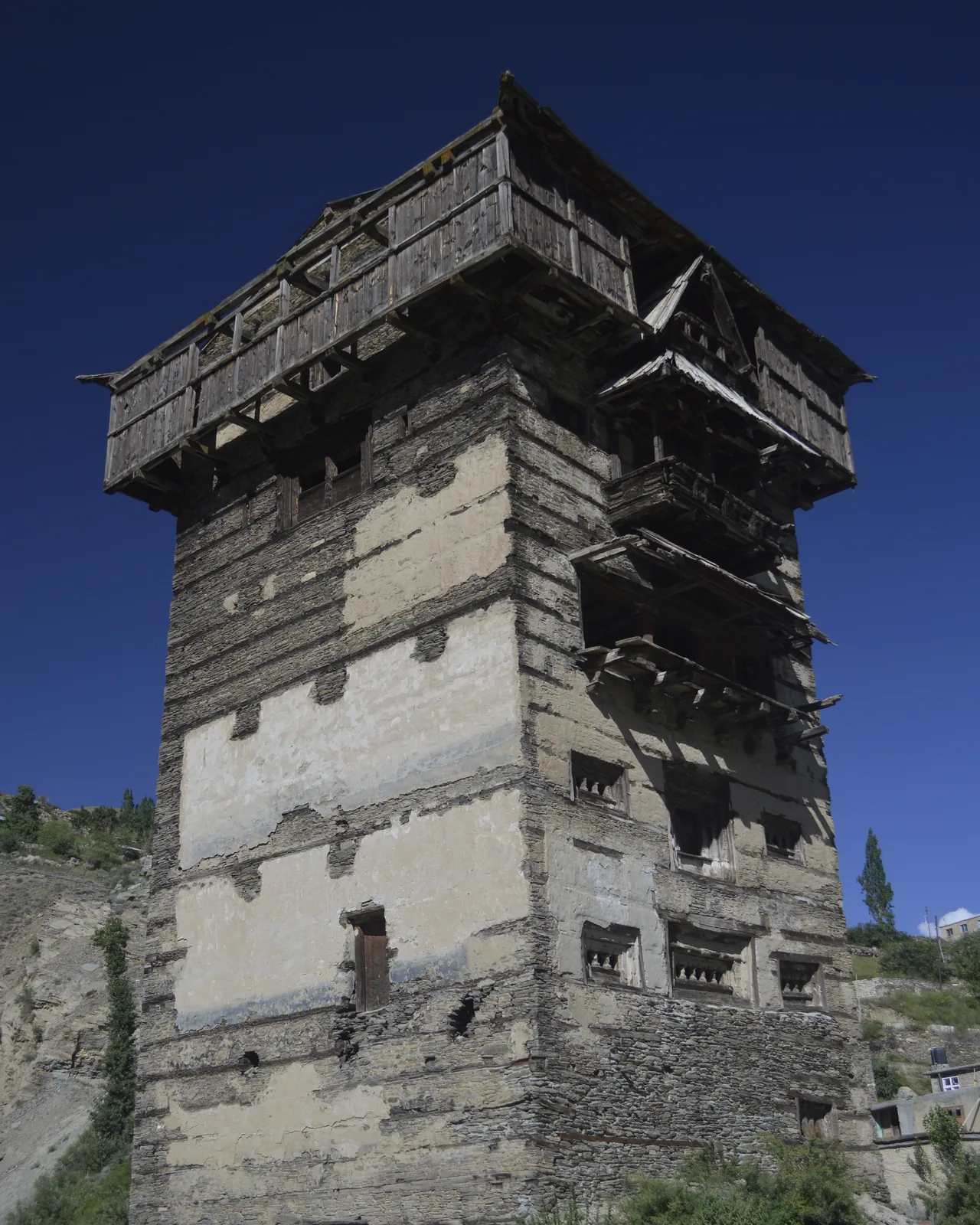 The tall stone-and-timber tower of Gondhla Fort in Lahaul, with a wooden balcony running around its top storey against a deep blue sky