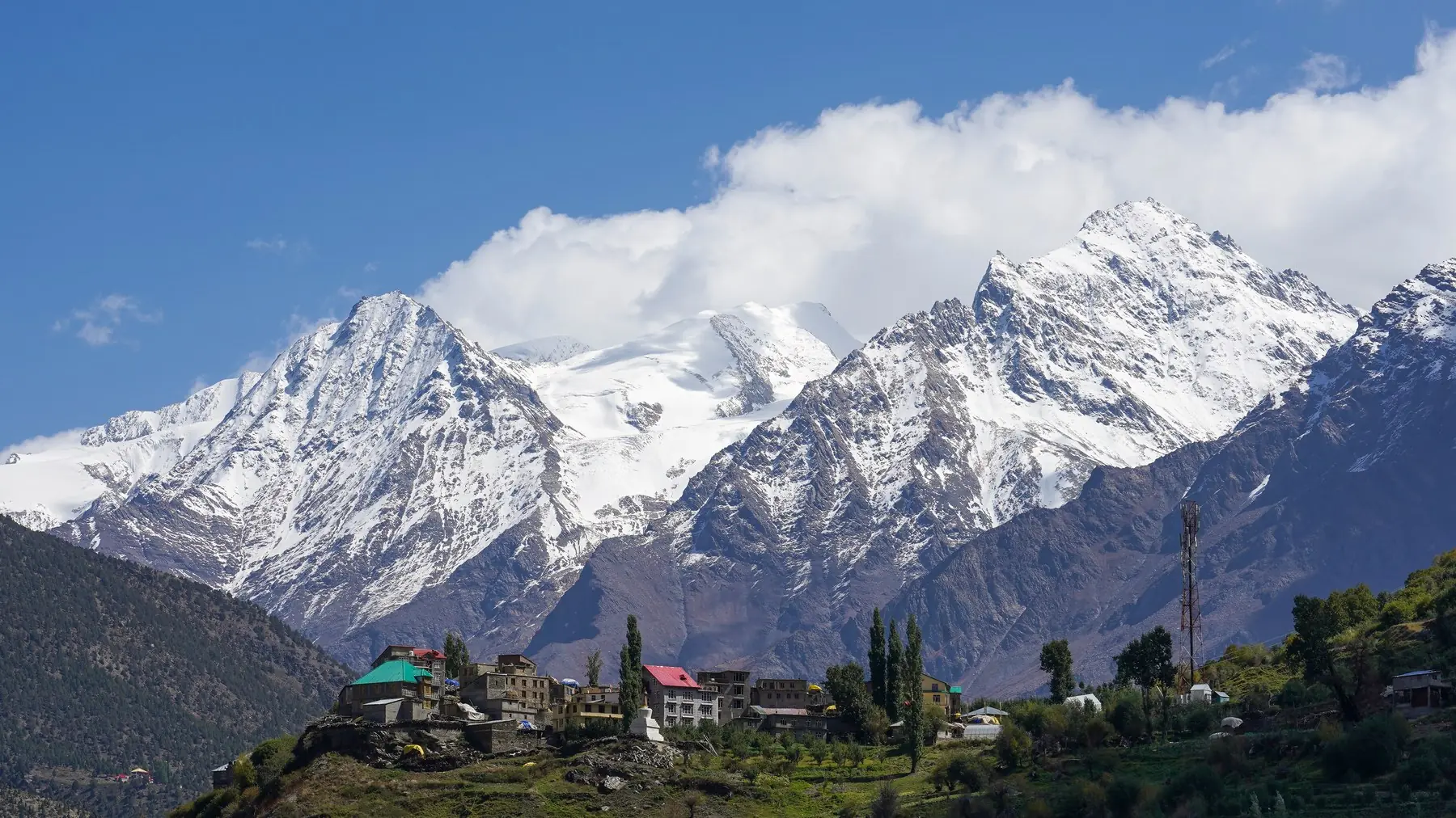 Kardang village on the slope across the Bhaga river from Keylong, with snow-covered Lahaul peaks behind, a destination for a self-drive car rental in Manali