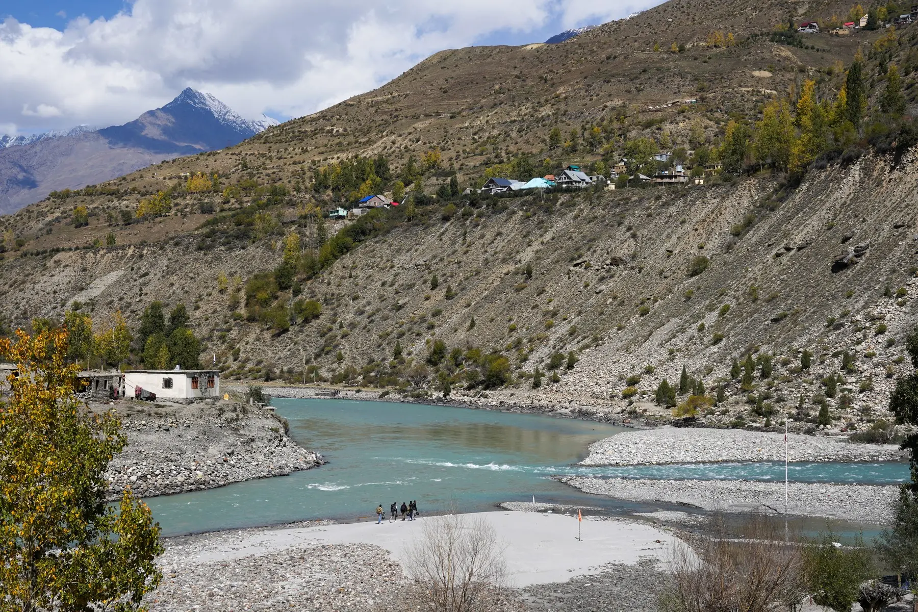 The turquoise Chandra and Bhaga rivers meeting at Tandi in Lahaul, with a wide gravel riverbed and autumn trees on the slope above