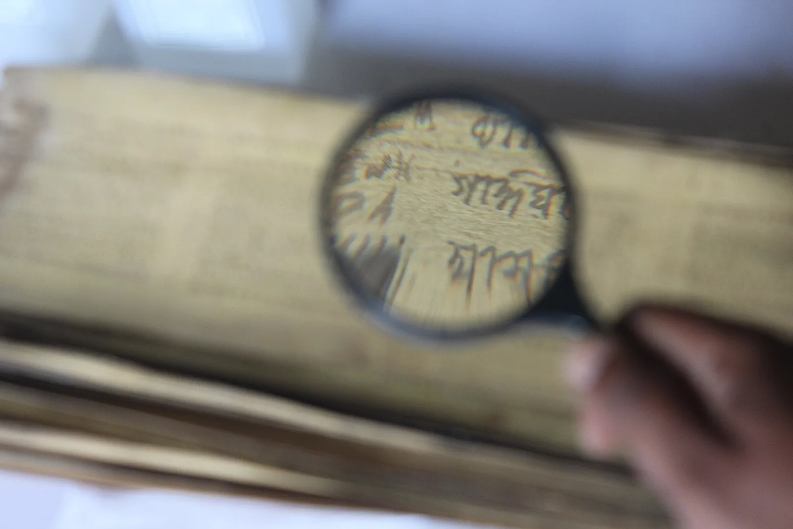 A magnifying glass held over the handwritten Assamese script of an old manuscript in the museum at Mayong
