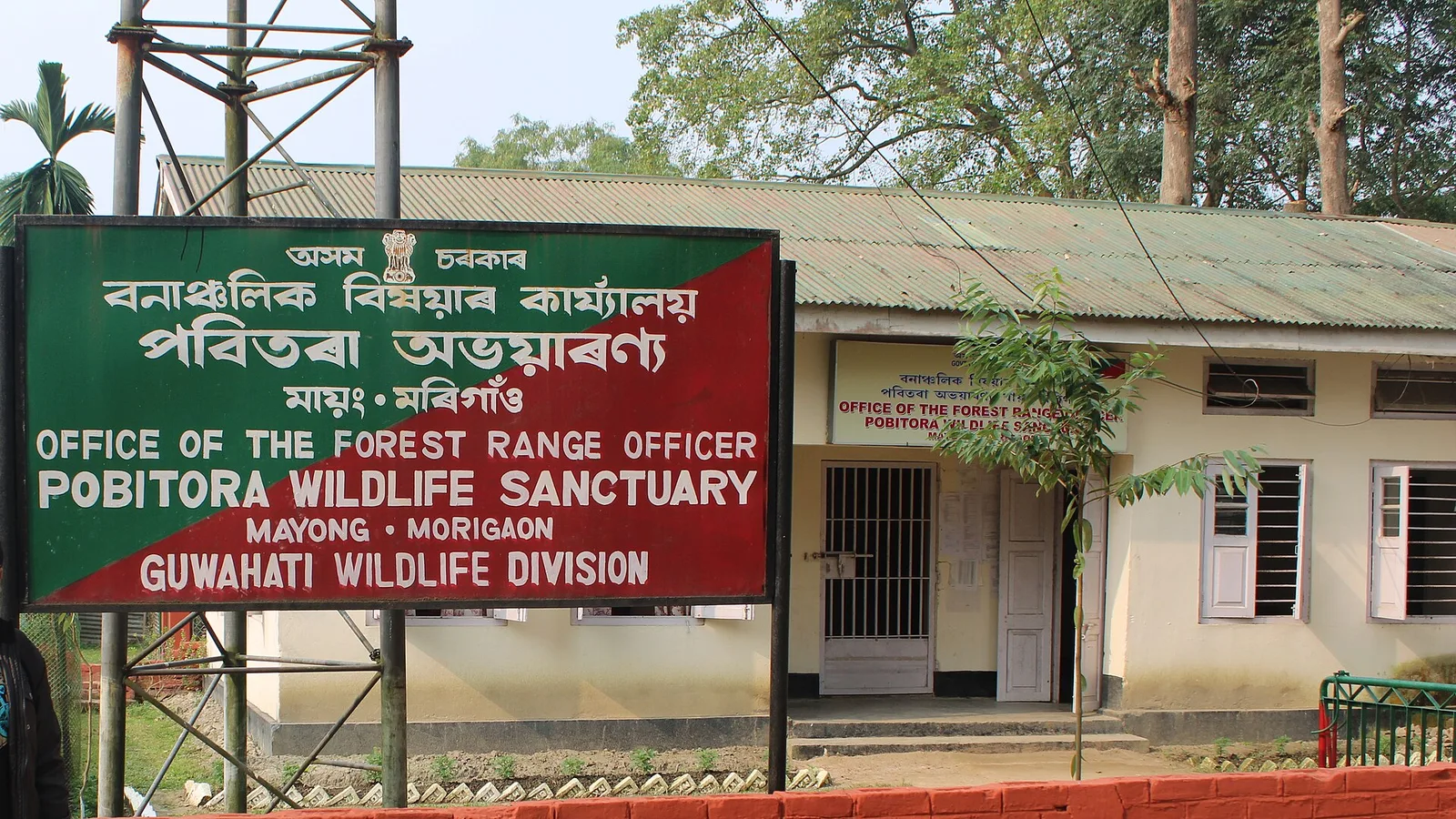 The green signboard of the Office of the Forest Range Officer, Pobitora Wildlife Sanctuary, Guwahati Wildlife Division, in front of the range office building