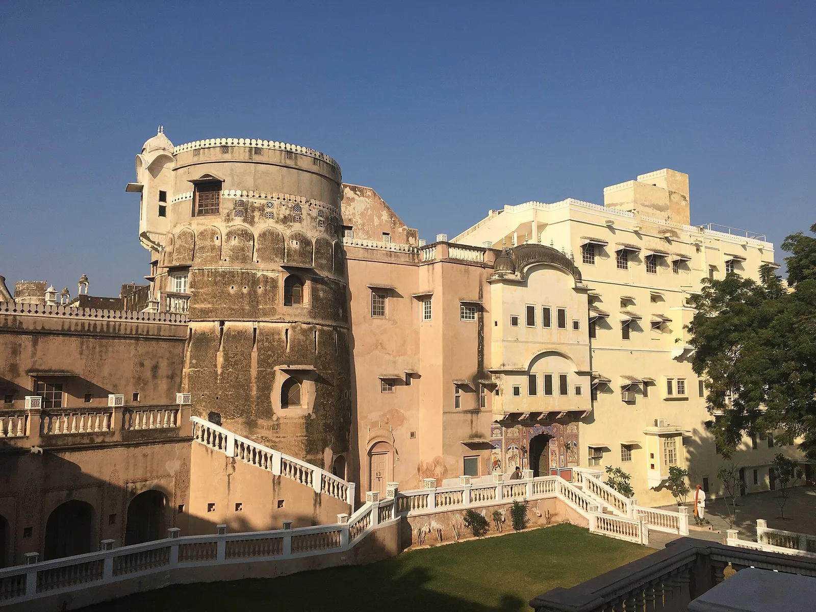 The round stone bastion and pale walls of Castle Mandawa under a clear blue sky, with white railings and a lawn in front