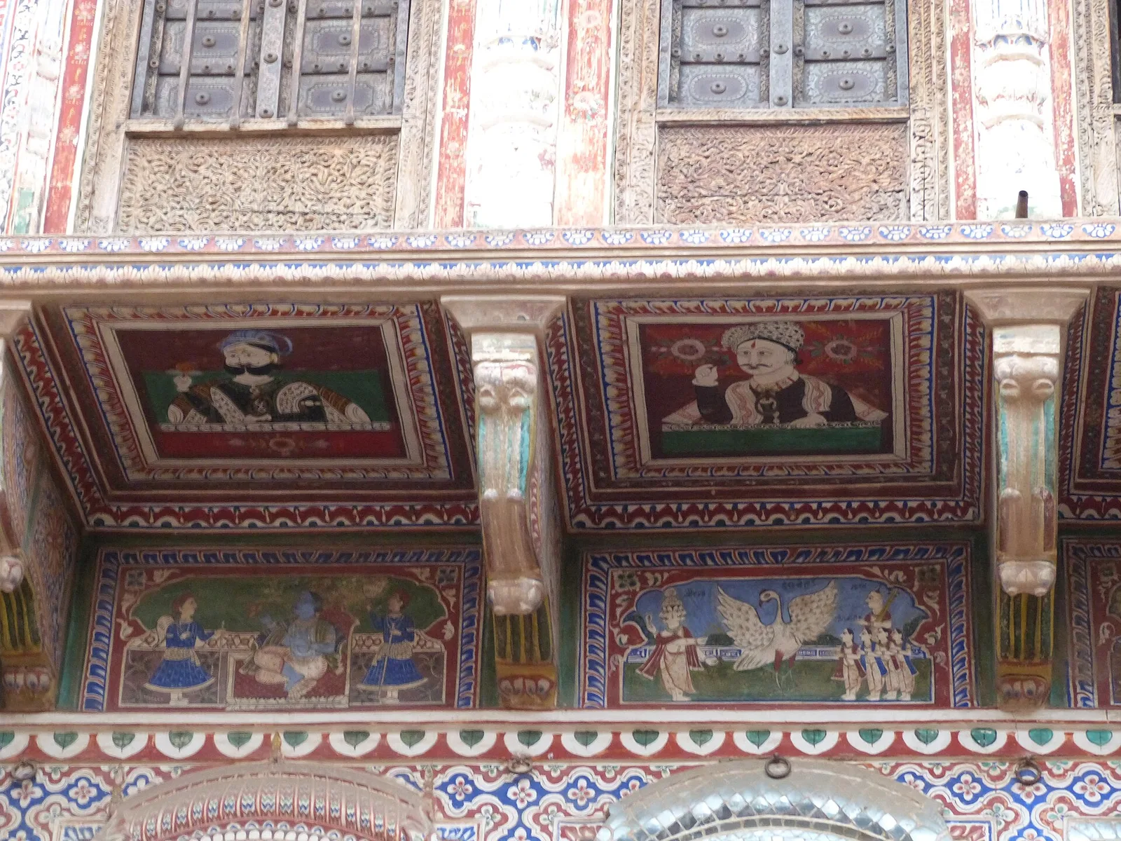 Painted fresco panels under the eaves of the Morarka Haveli in Nawalgarh, showing portraits, deities and a winged figure in red, blue and green