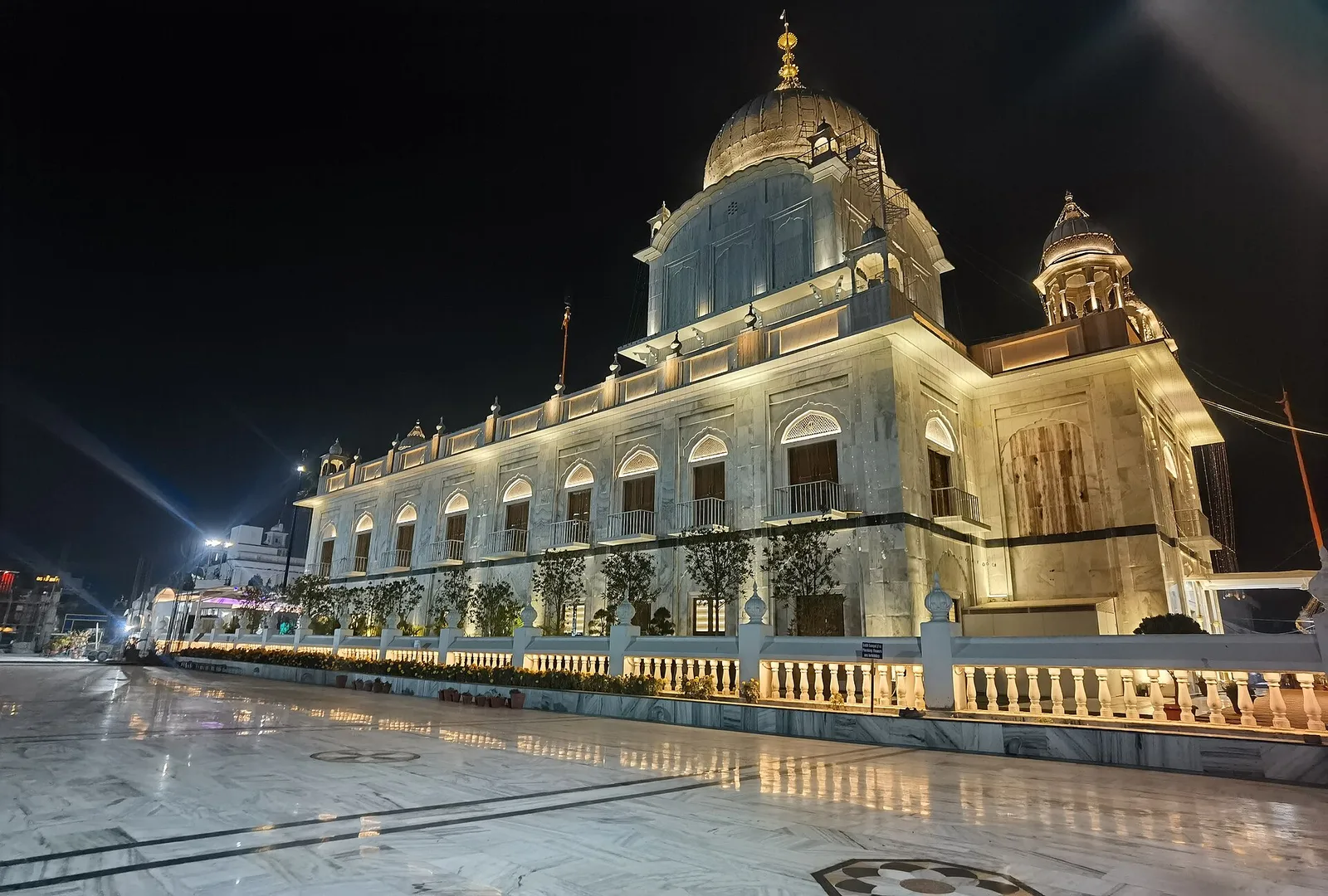 Gurdwara Paonta Sahib lit up at night, a white building with a gilded dome, arched windows and a marble courtyard