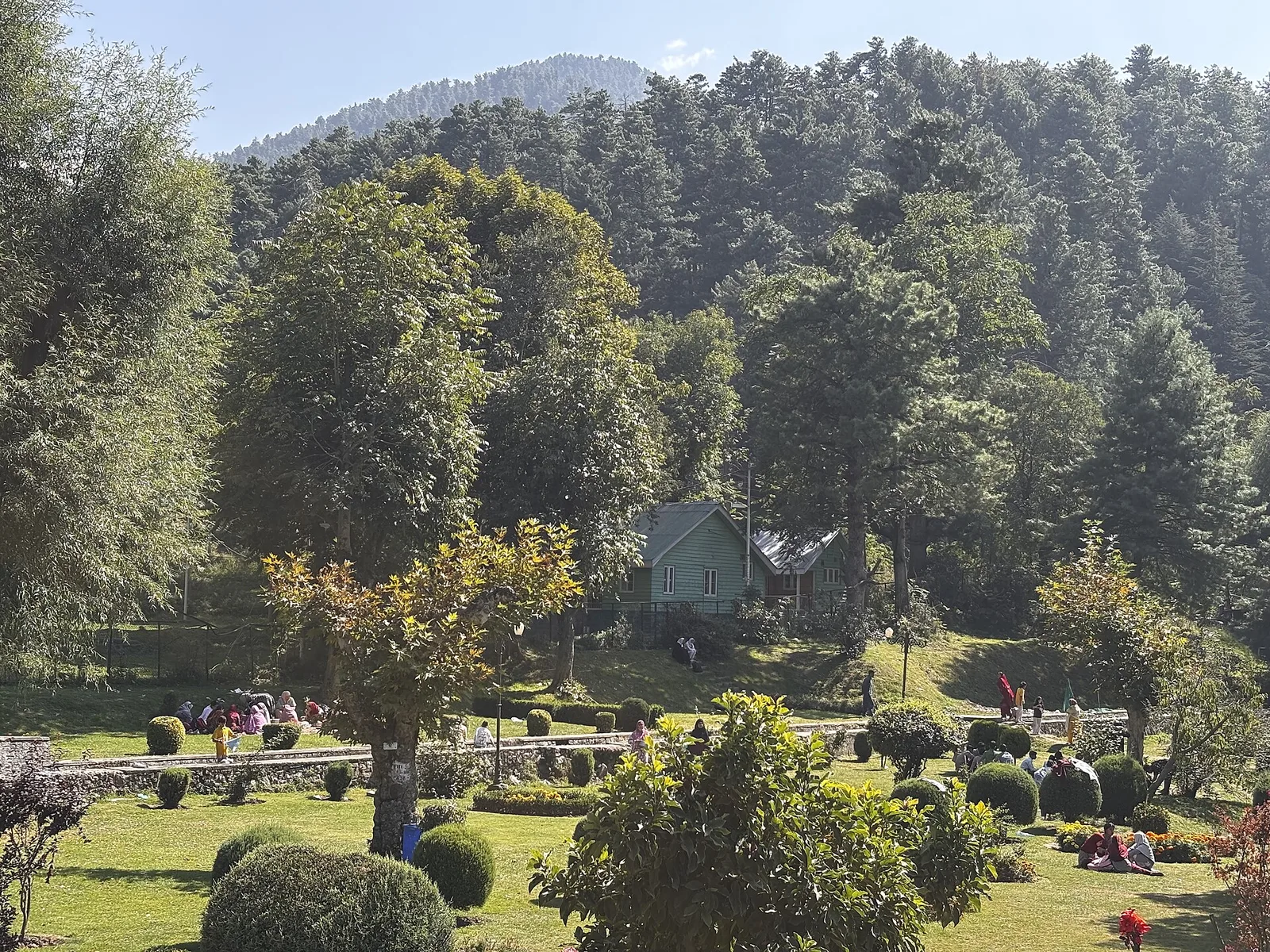 The botanical garden at Kokernag with clipped shrubs, flower beds and a cottage beneath a pine-covered hill