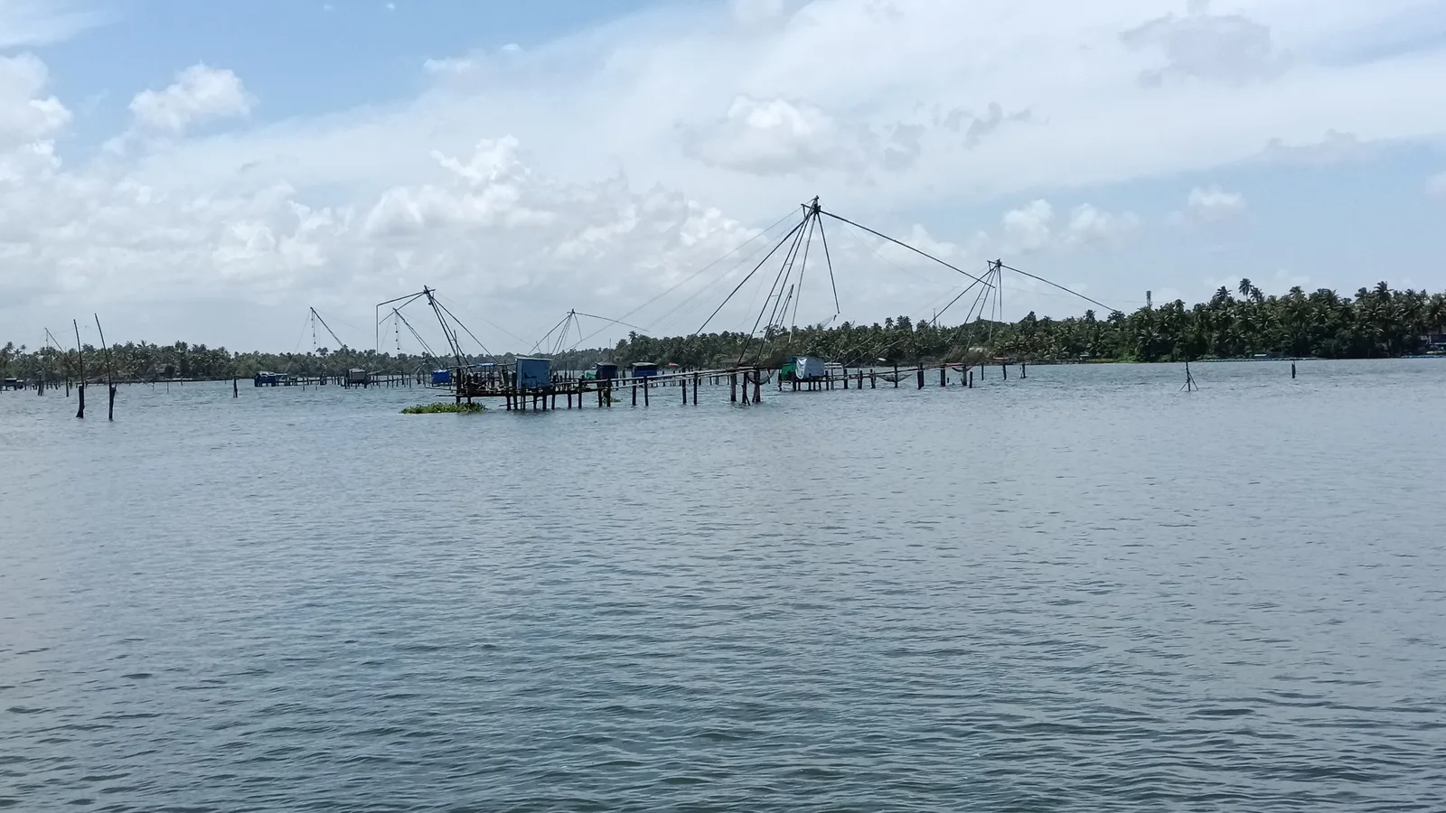 Chinese fishing nets standing in the wide Periyar near Kottappuram Fort under a cloudy sky, the end of a bike rental in Cochin ride to Muziris