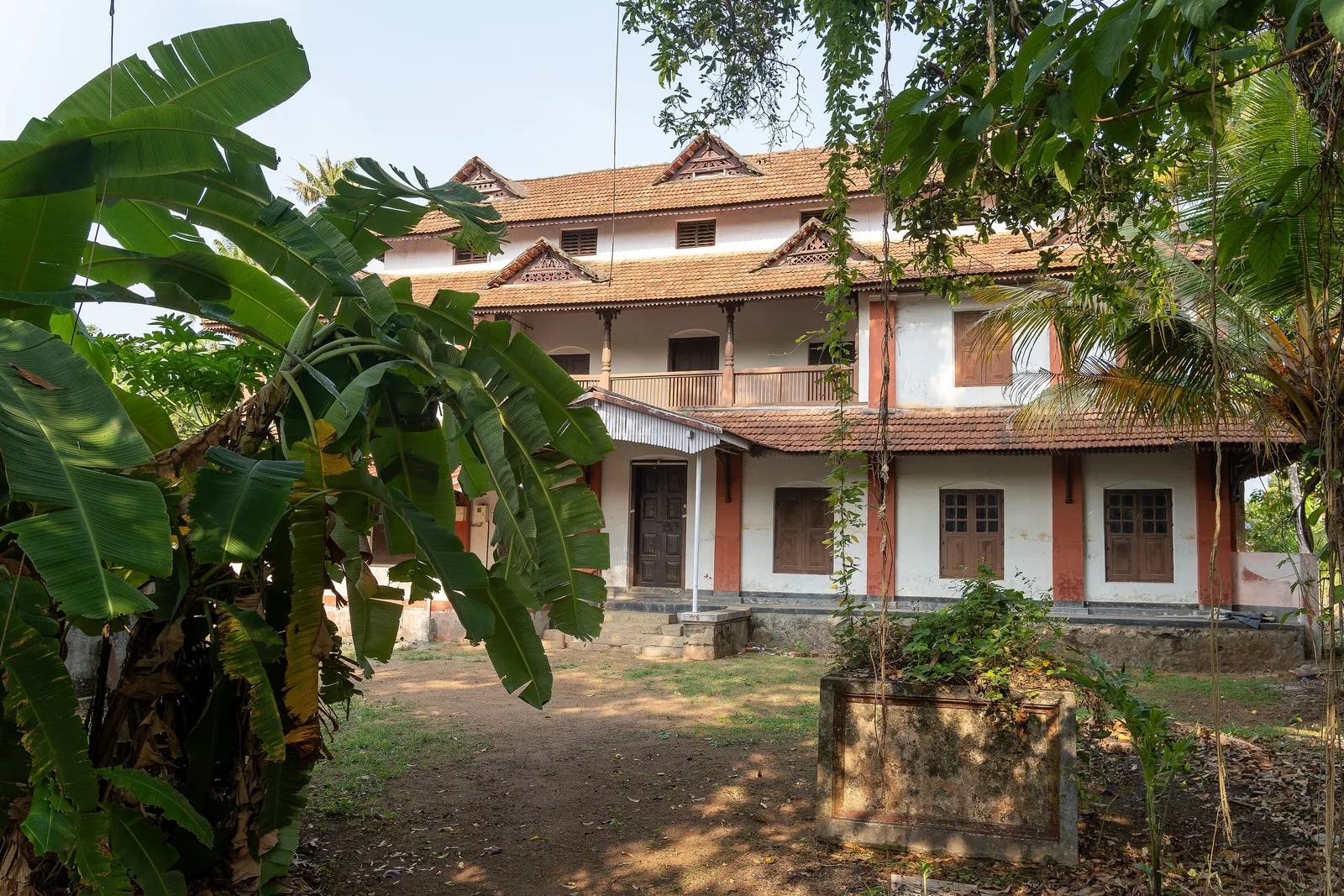 A two-storey tiled-roof building of the Paliam palace complex at Chendamangalam, seen past banana leaves