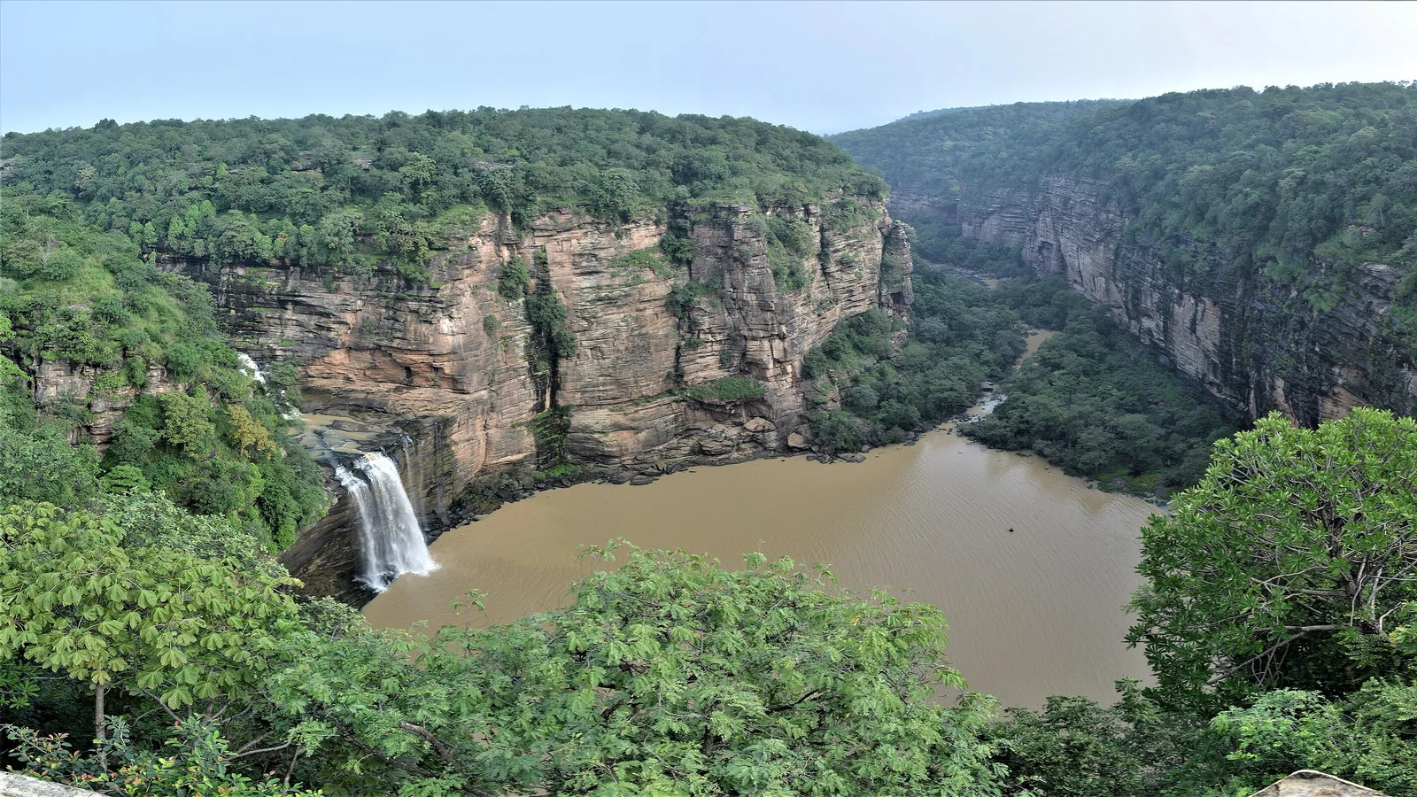 Devdari waterfall dropping into a muddy pool below sandstone cliffs and forest in Chandraprabha Wildlife Sanctuary, a day trip by self-drive car rental in Varanasi