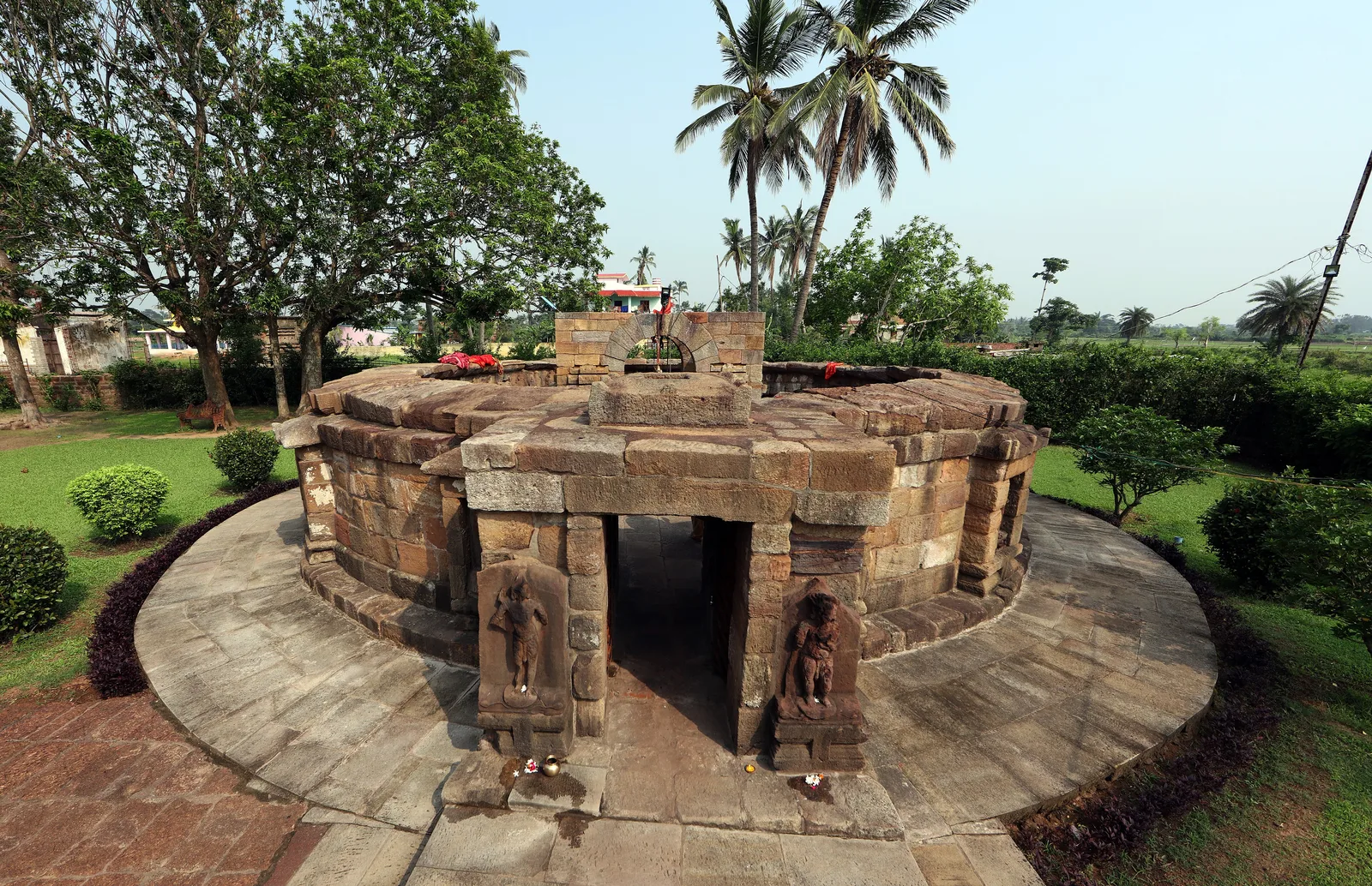 The small, circular, roofless Chausathi Yogini temple at Hirapur, built of sandstone blocks, with a narrow entrance and palm trees behind it