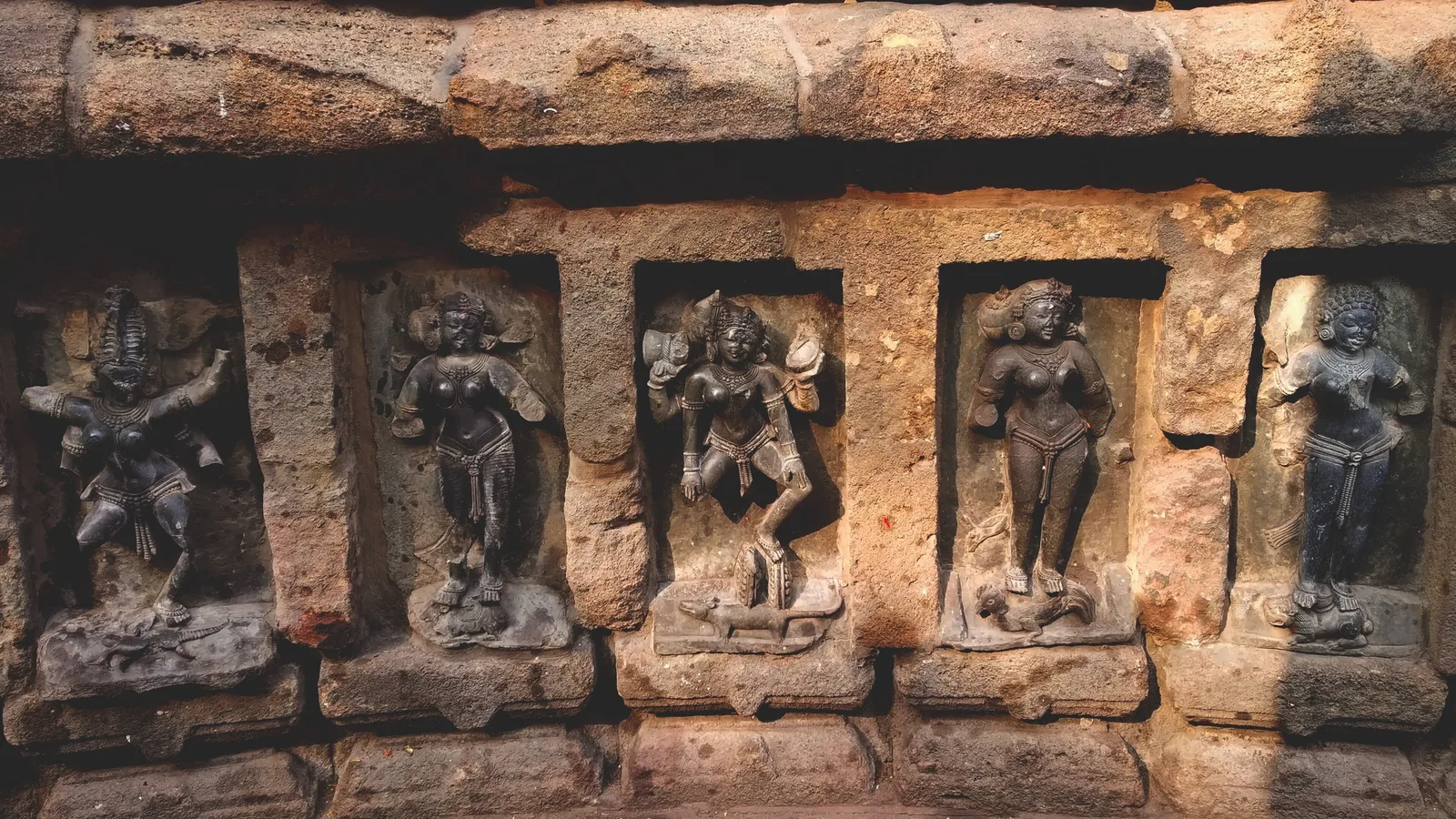 Five carved yogini figures in dark stone standing in their niches inside the circular wall of the Hirapur temple