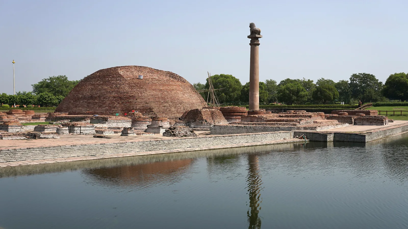 The brick stupa and the polished Ashokan lion pillar at Kolhua, Vaishali, reflected in the ancient tank in front of them, a day trip by self-drive car rental in Patna