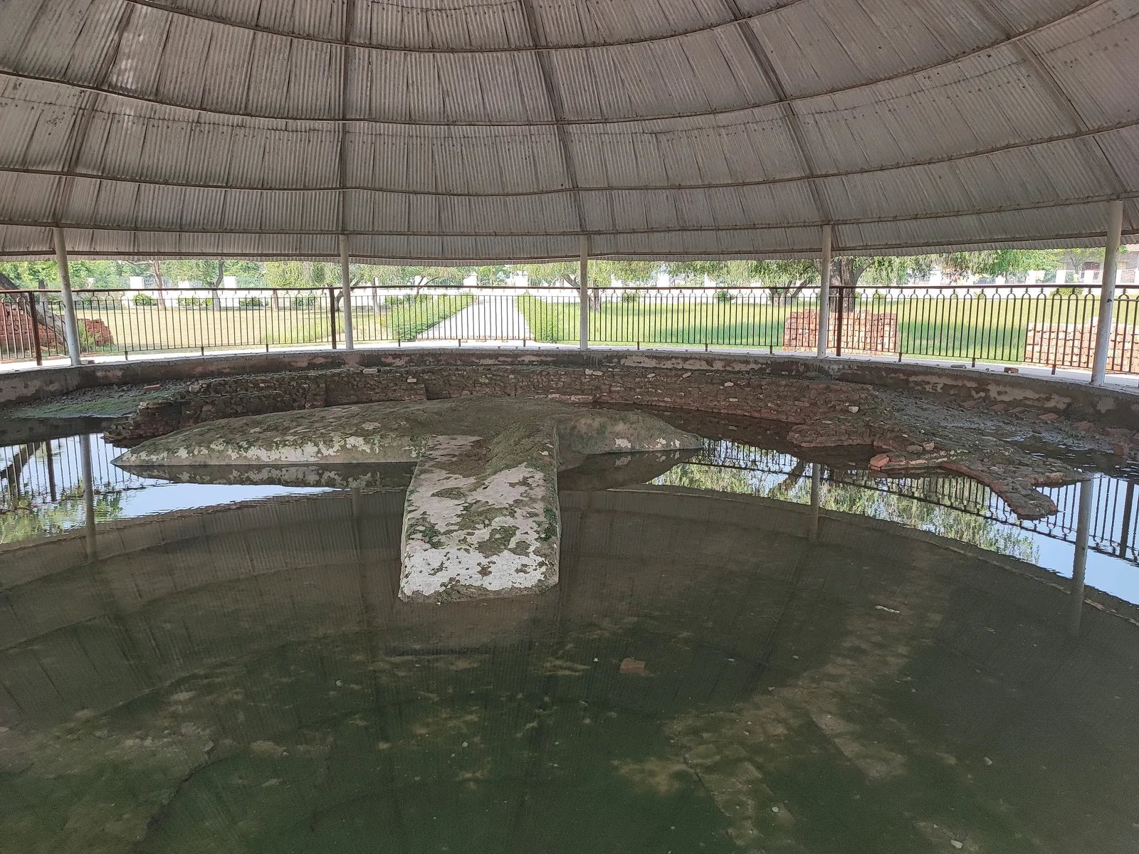 The remains of the Buddha Relic Stupa at Vaishali, a low circular mud and brick base under a round protective canopy, with water collected around it
