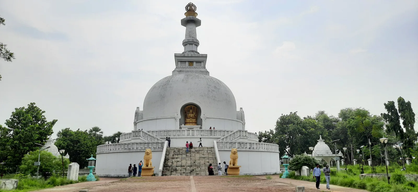 The white dome of the Vishwa Shanti Stupa, the World Peace Pagoda at Vaishali, with a golden Buddha in its niche, a wide stairway and lion statues at the base