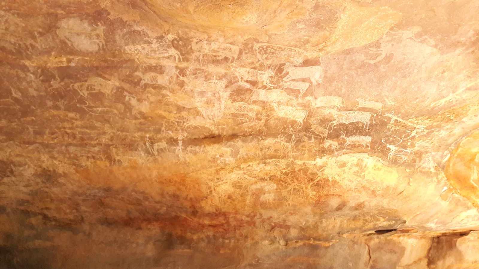Prehistoric rock paintings in red and white on a sandstone wall at the Bhimbetka rock shelters, a short drive by self-drive car rental in Bhopal