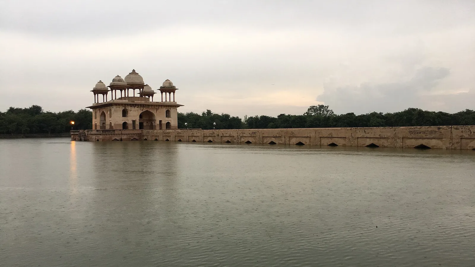 Narnaul's Jal Mahal, a domed Mughal pavilion on an arched causeway, standing in a full reservoir under a cloudy sky, a day trip by self-drive car rental in Delhi