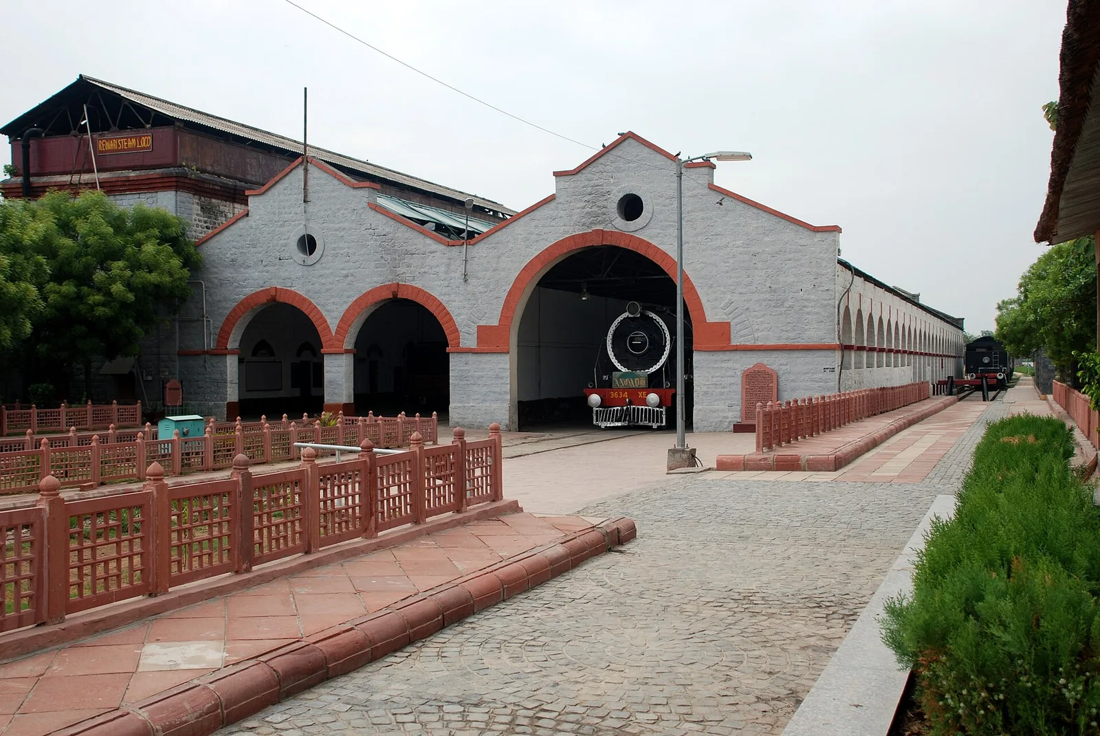 The whitewashed Rewari heritage steam loco shed with red-trimmed arches and a black steam locomotive parked in the central bay