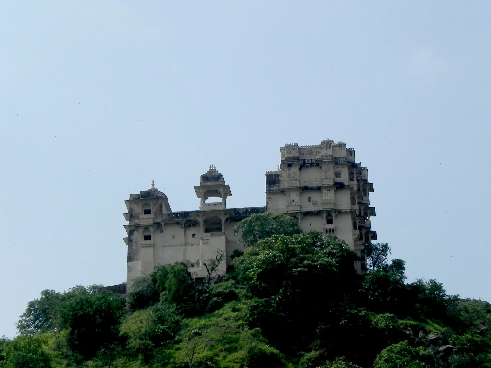 Hawa Mahal at Jaisamand, a tall stone palace with domed corner towers on a wooded hilltop above the lake