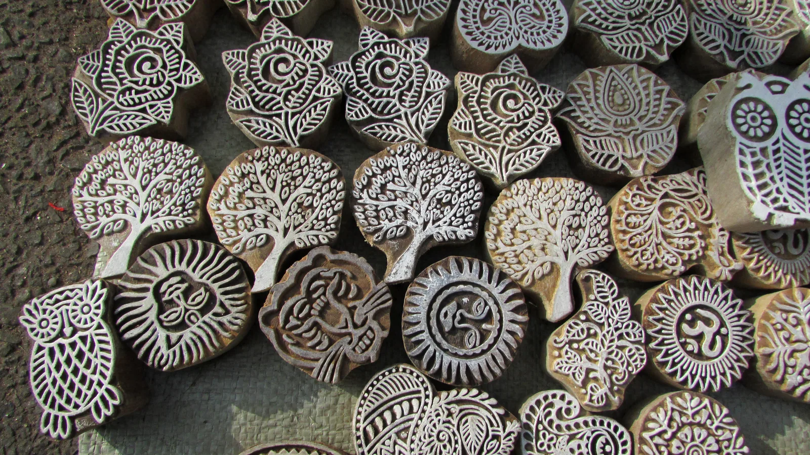 Dozens of carved wooden printing blocks with tree, flower, sun and owl designs laid out together, used for hand block printing near Jaipur