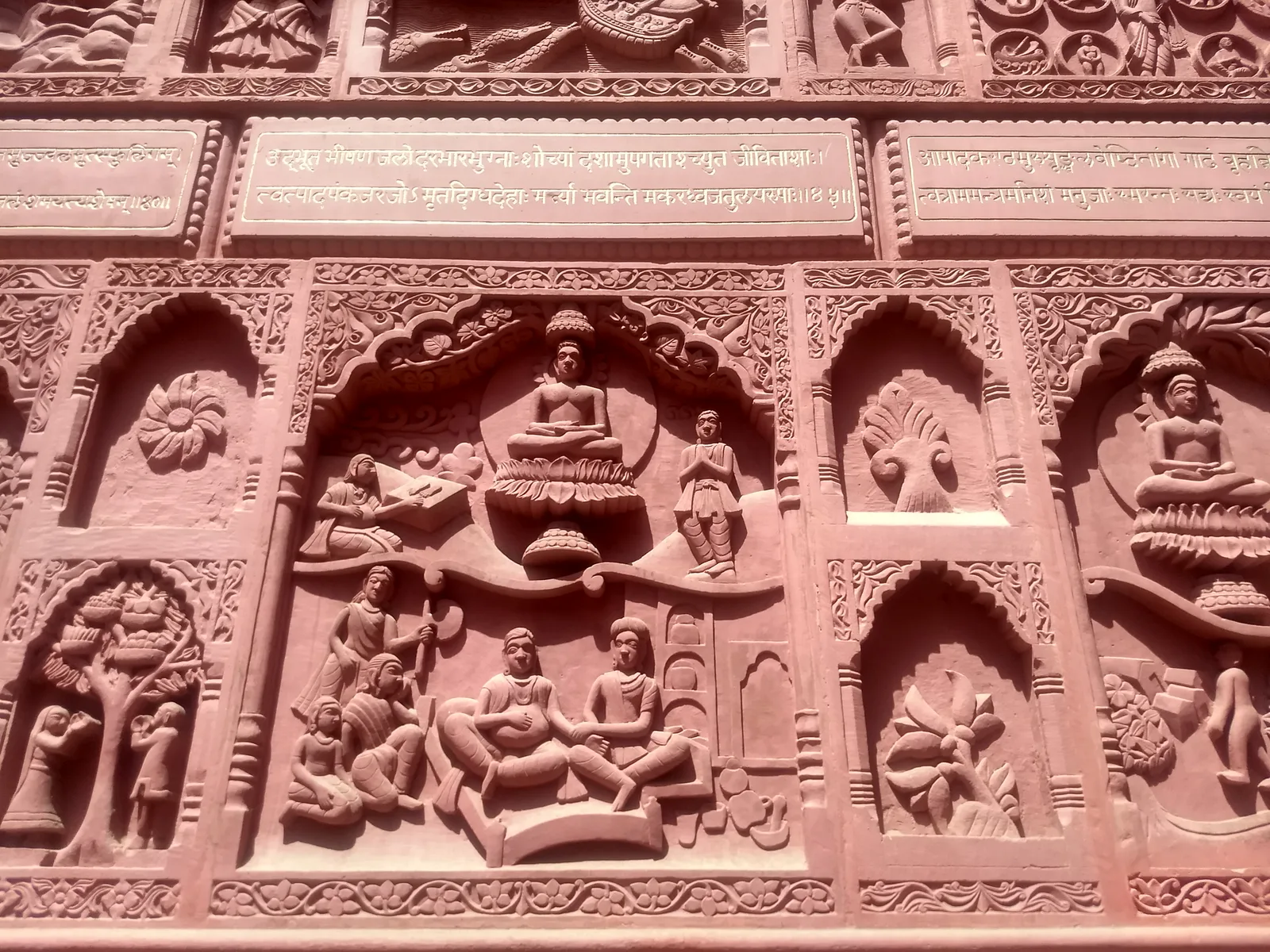Close view of carved red sandstone panels on the wall of the Sanghiji Jain temple in Sanganer, showing seated figures in arched niches