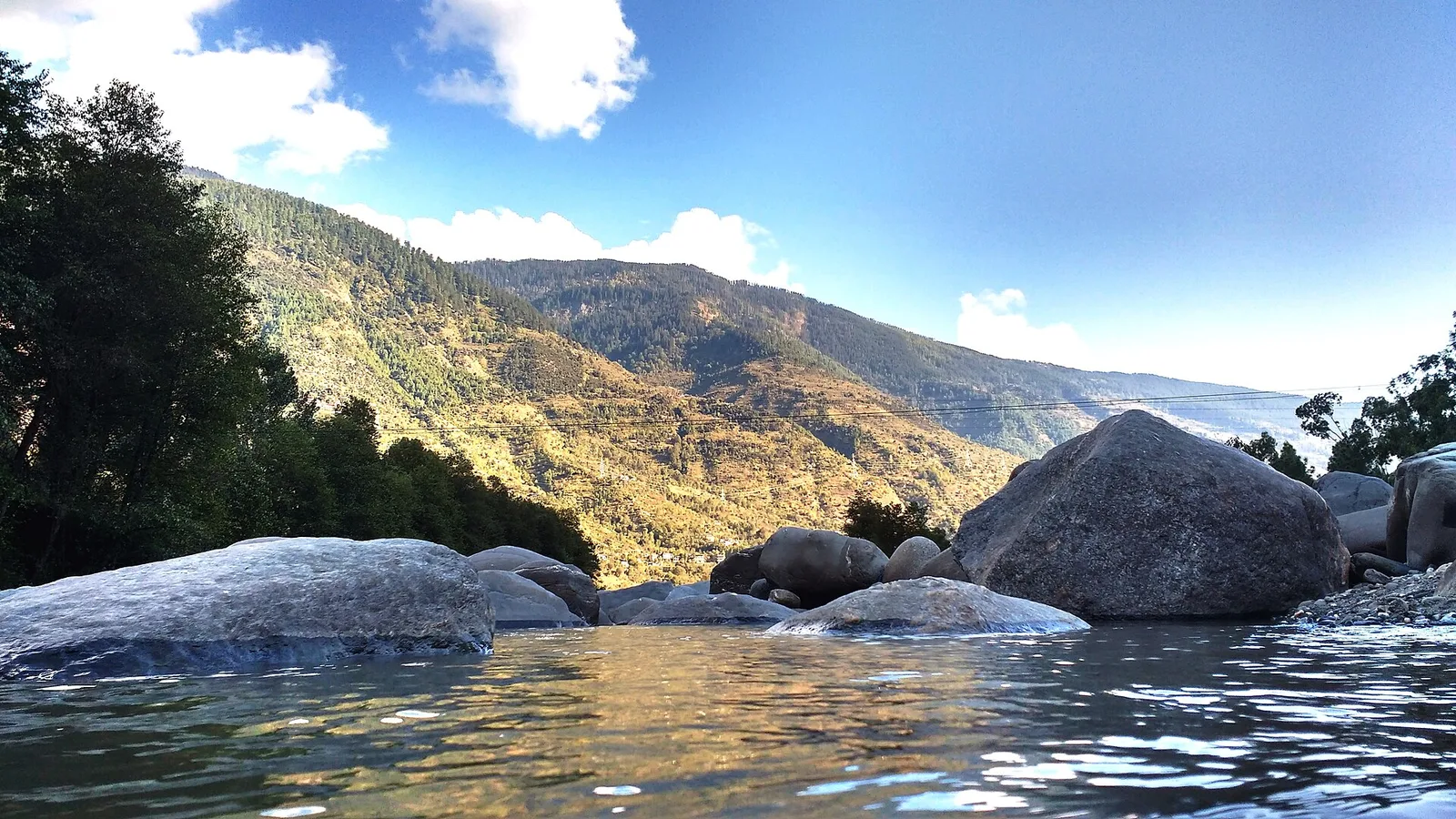 The Beas river flowing over boulders through the green Kullu valley in Himachal Pradesh